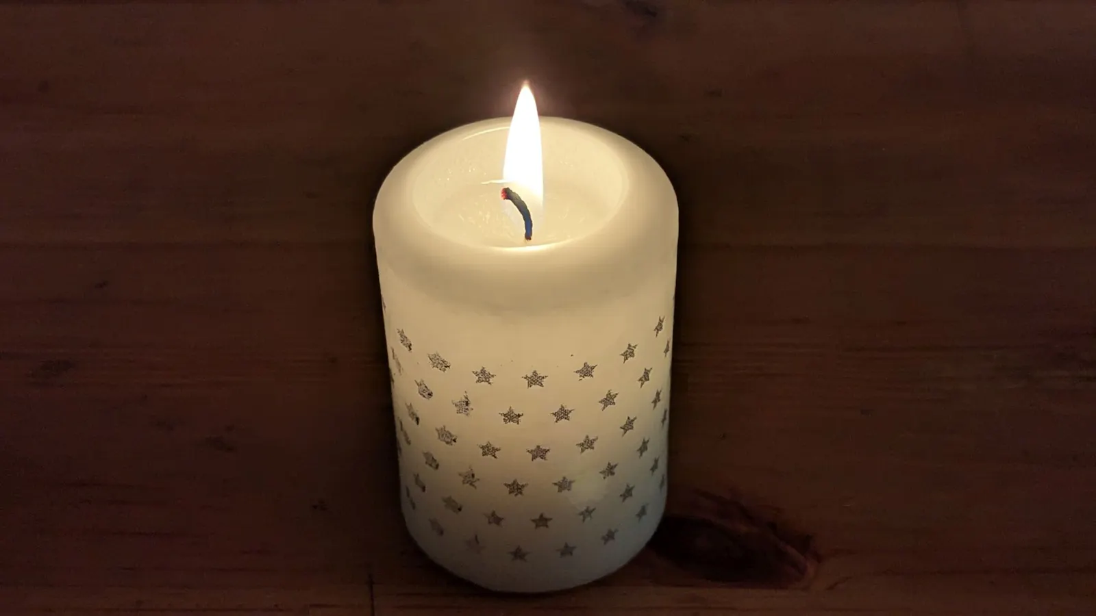 Eine Kerze mit aufgeklebten Sternchen leuchtet im Dunkeln.