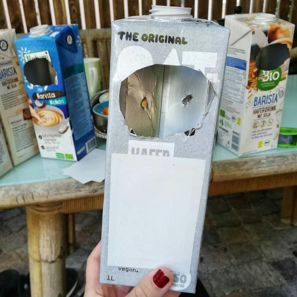 Eine Menge an bearbeiteter Getränkekartons stehen auf einem Tisch. Die Kippenbox im Vordergrund hat eine große Öffnung, hoffentlich stopft niemand etwas großes hinein...