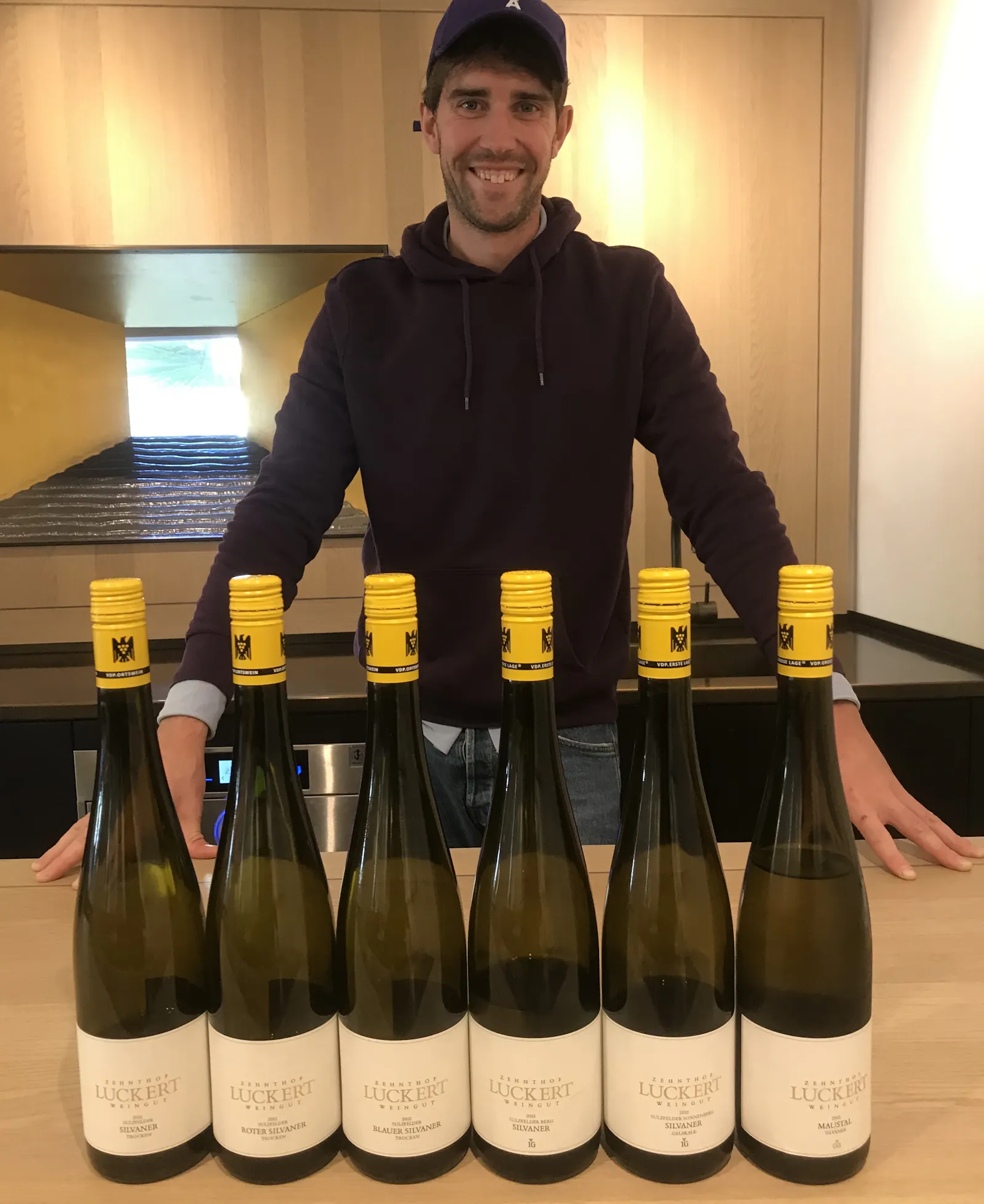 Philipp Luckert steht hinter einem Trsen, auf dem sechs Weinflaschen stehen