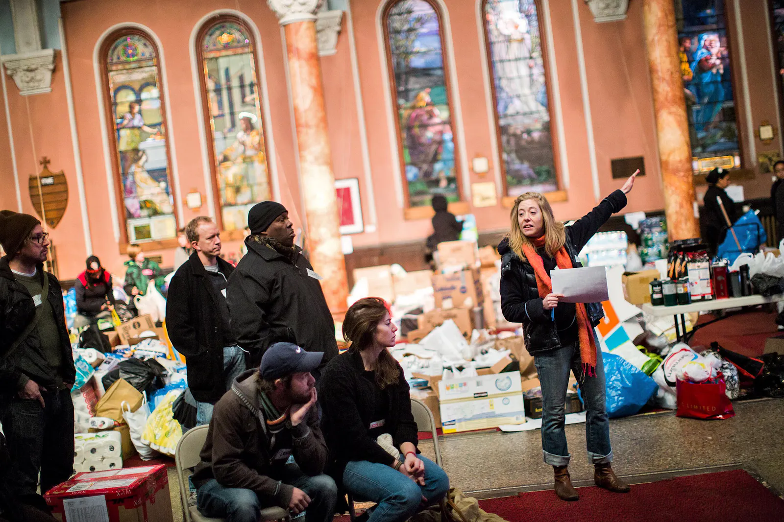 Bild der Occupy-Sandy-Bewegung, Frau in oranger Weste weist betroffenen Menschen den Weg, Ort: Kirche, gefüllt mit verschiedenen Kisten und Spenden
Foto: Piotr Redlinski for The New York Times