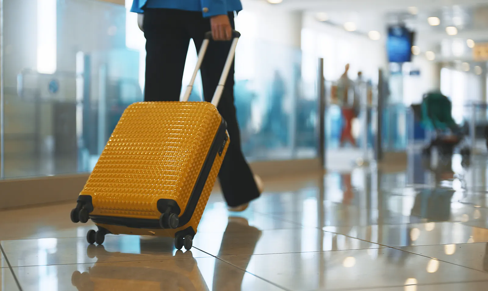Das Bild zeigt eine Person, die einen gelben Trolley durch einen Flughafen zieht.