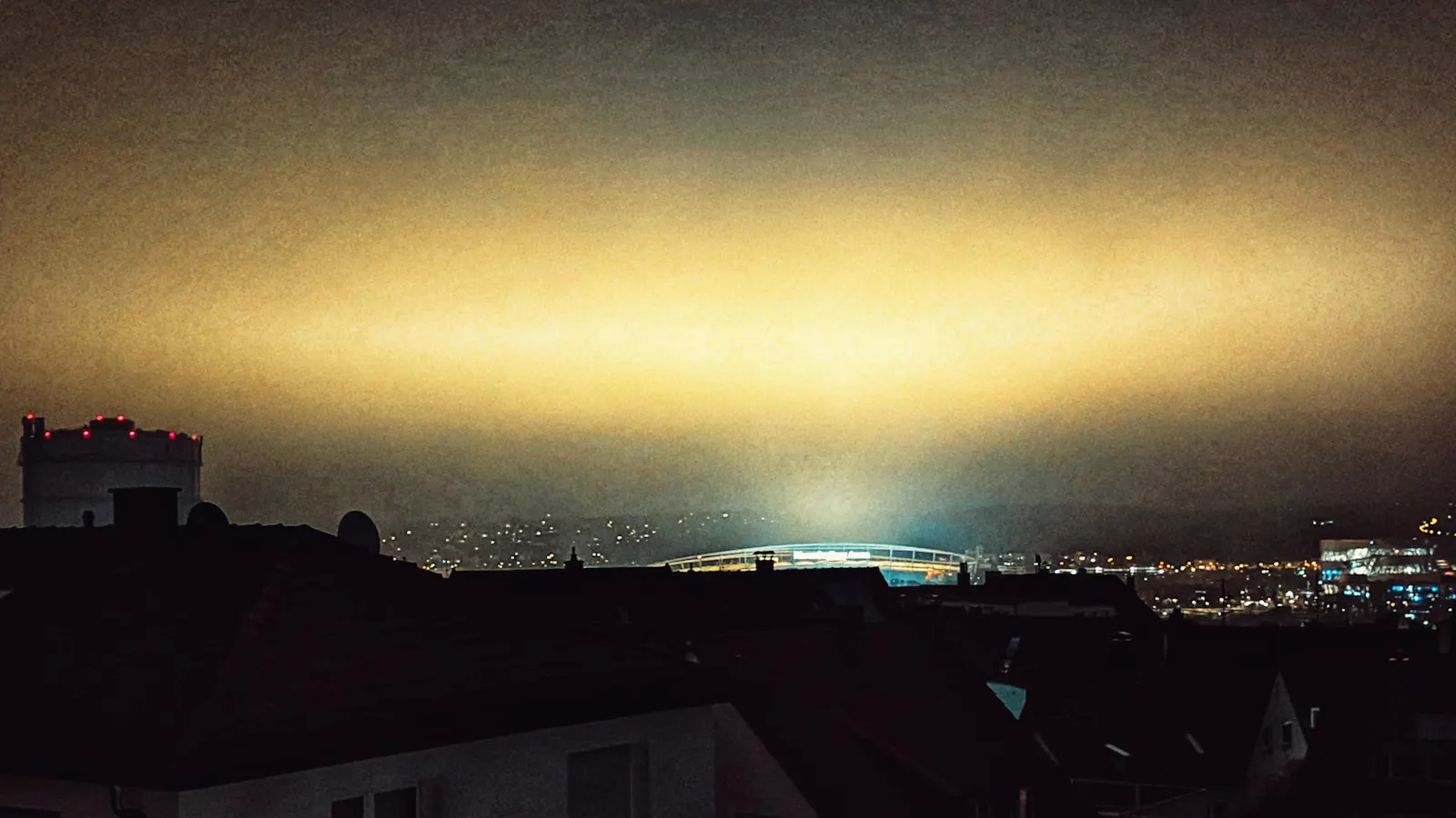 Symbolbild: Lichtschein über der Mercedes-Benz-Arena bei Nacht, links der Gaskessel, rechts das Mercedes-Benz-Museum. Foto: Jürgen Brand