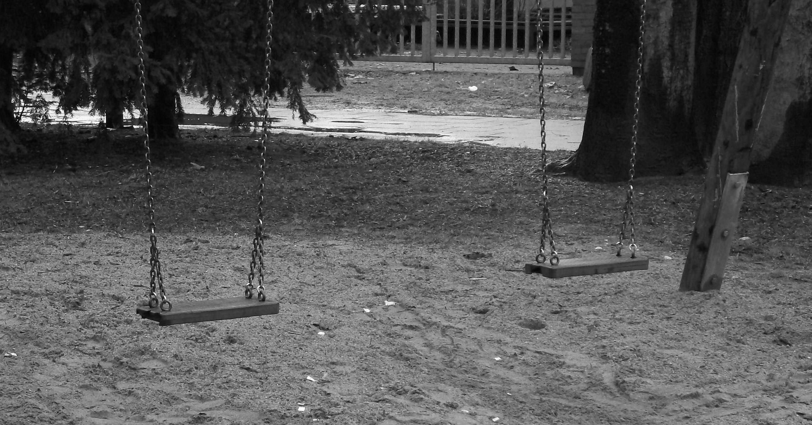 Schwarz-Weiß-Foto eines Spielplatzes mit zwei leeren Schaukeln.