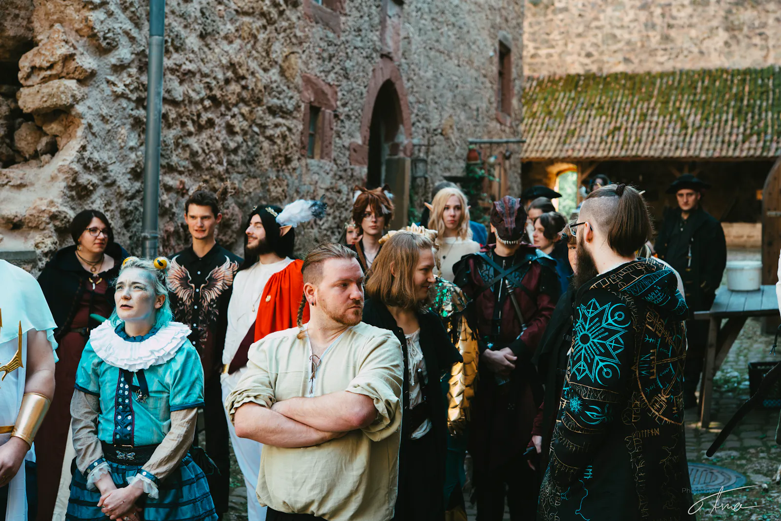 Eine große Gruppe von Helden geht durch den Innenhof der Burg. Alle sind in unterschiedlichsten Gewandungen gekleidet.