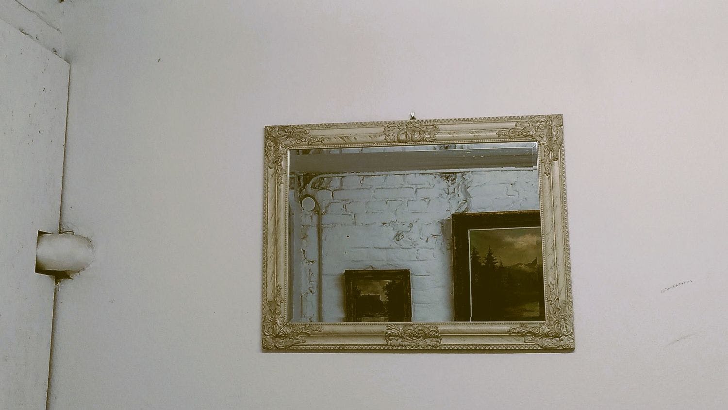 In einem Spiegel an der Wand spiegeln sich Gemälde verschiedener Größe.