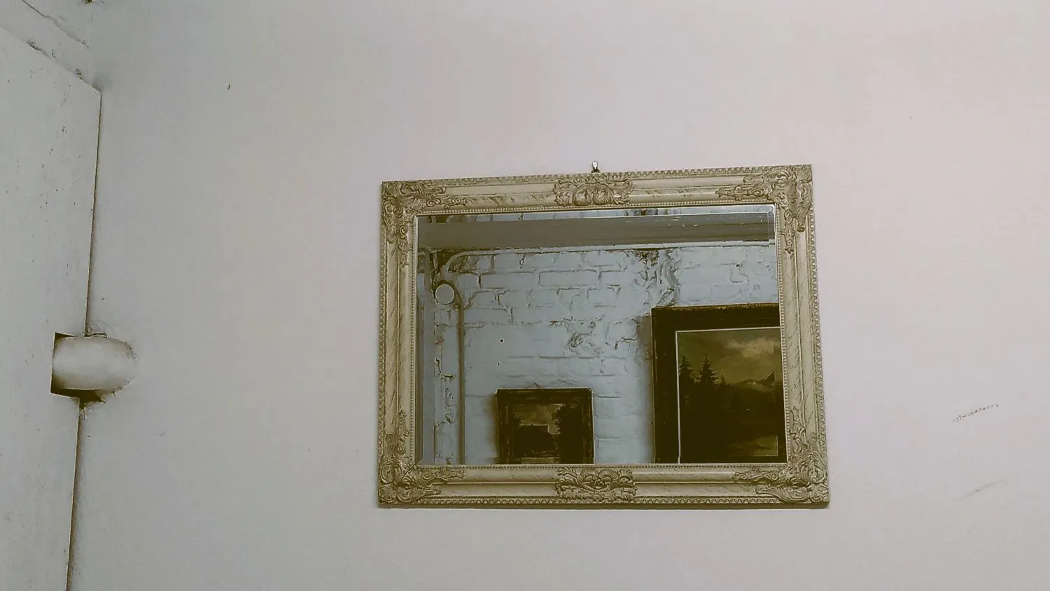 In einem Spiegel an der Wand spiegeln sich Gemälde verschiedener Größe.