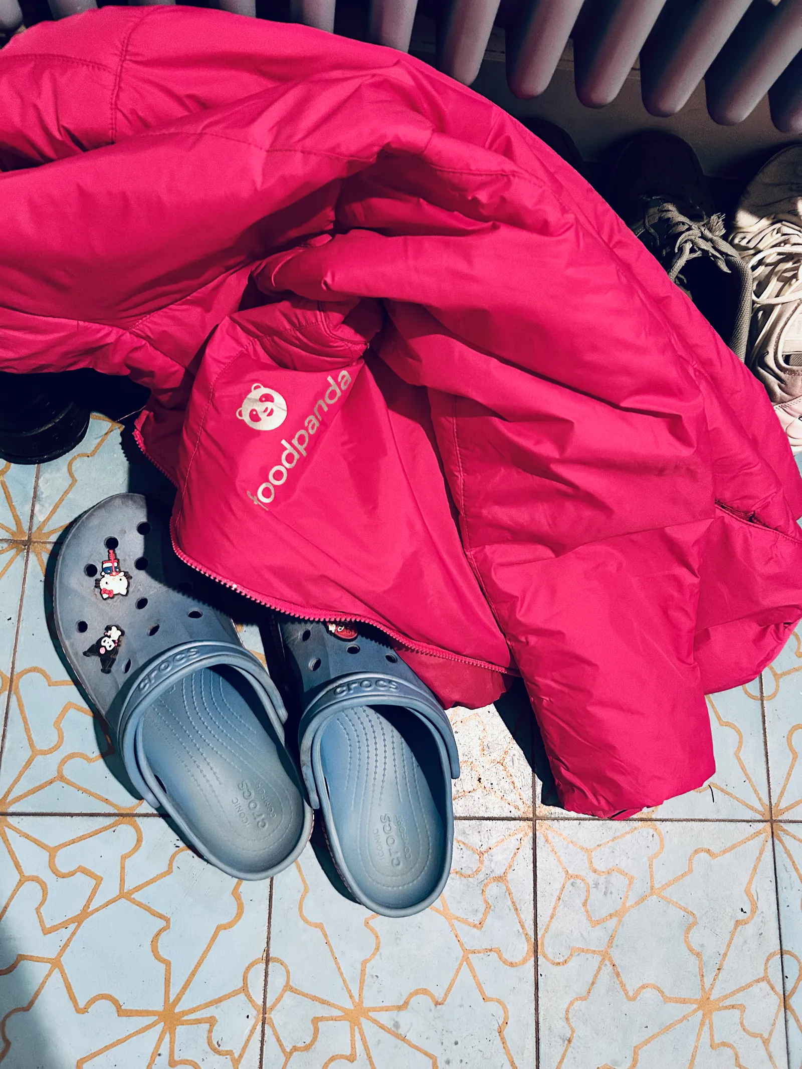 Foodpanda-Jacke liegt auf hellblauen Croqs mit Hello-Kitty-Pins