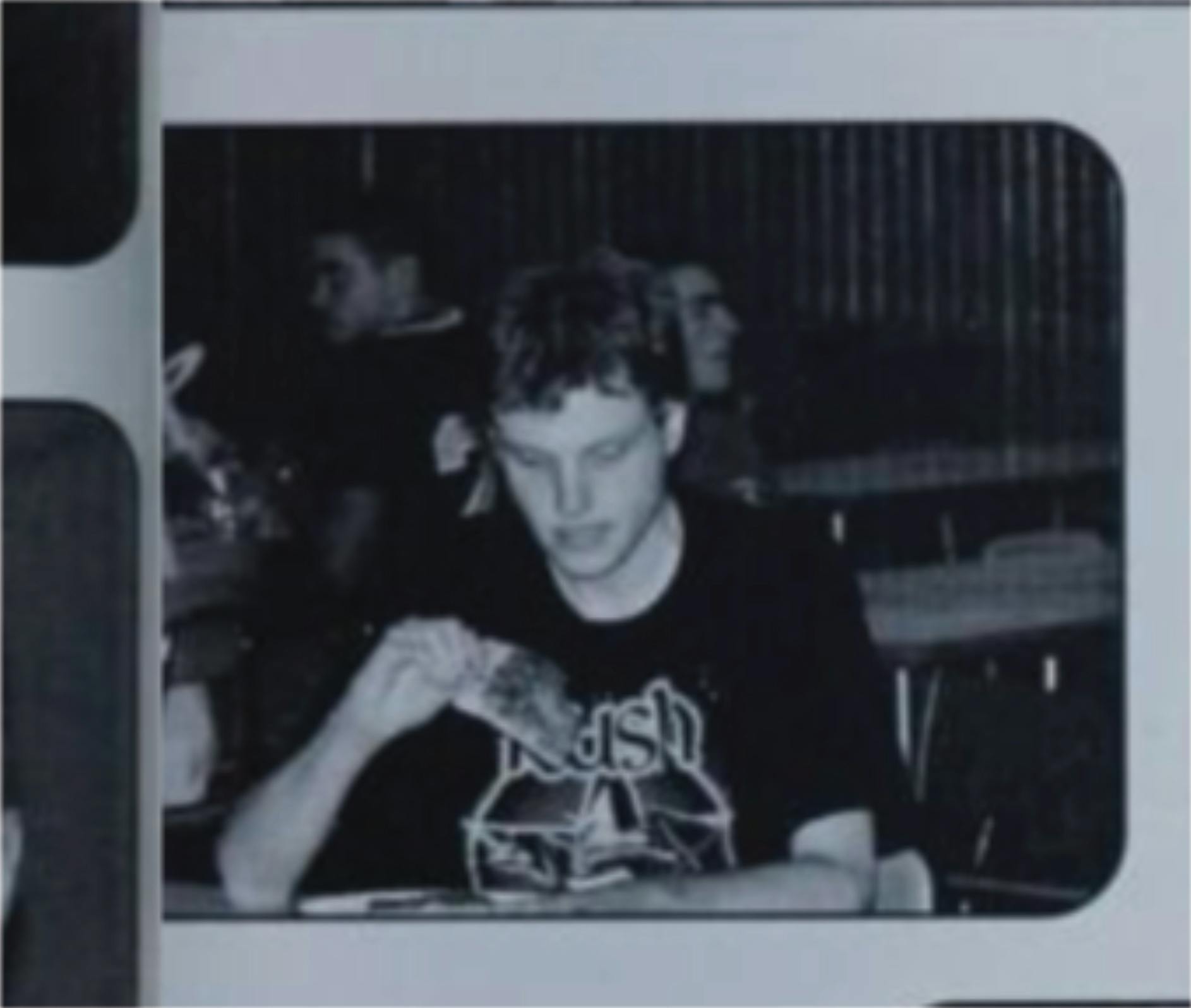 A monochrome picture of me taken candidly my senior year. I'm not aware of the photo being taken and am looking glumly at a slice of pizza. I am wearing, appropriately, a Rush T-shirt from the 30th anniversary tour because it was an out of uniform day. I am completely alone at my table.