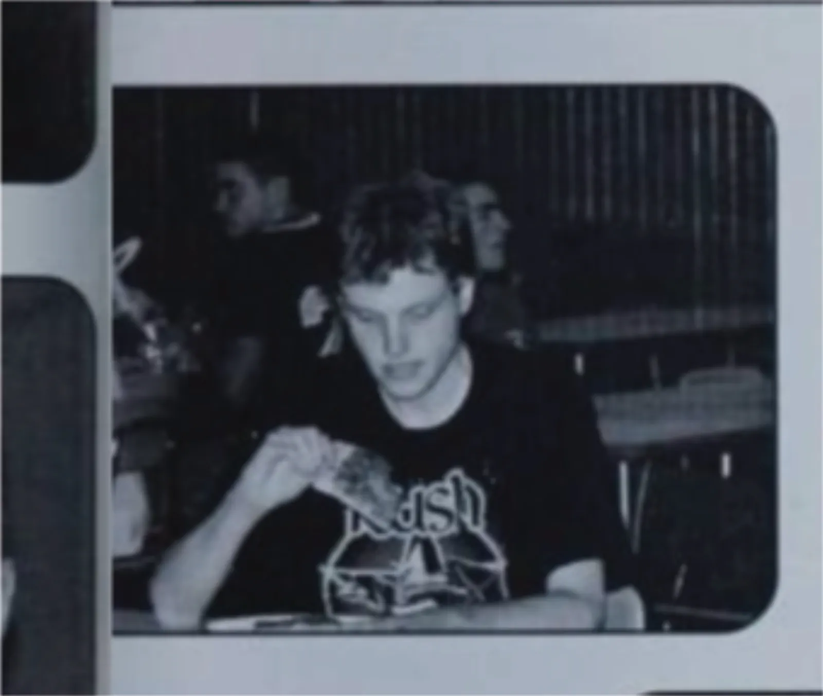 A monochrome picture of me taken candidly my senior year. I'm not aware of the photo being taken and am looking glumly at a slice of pizza. I am wearing, appropriately, a Rush T-shirt from the 30th anniversary tour because it was an out of uniform day. I am completely alone at my table.