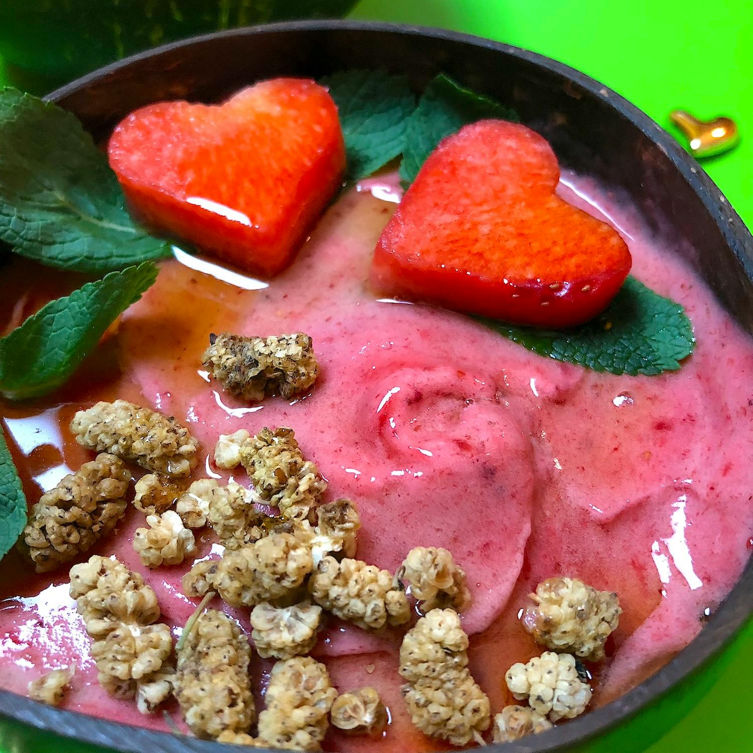 Erdbeeren - Bananen Eis in Kokos Schälchen, dekoriert mit Minzen Blättchen und getrockneten Maulbeeren und etwas Ahornsirup