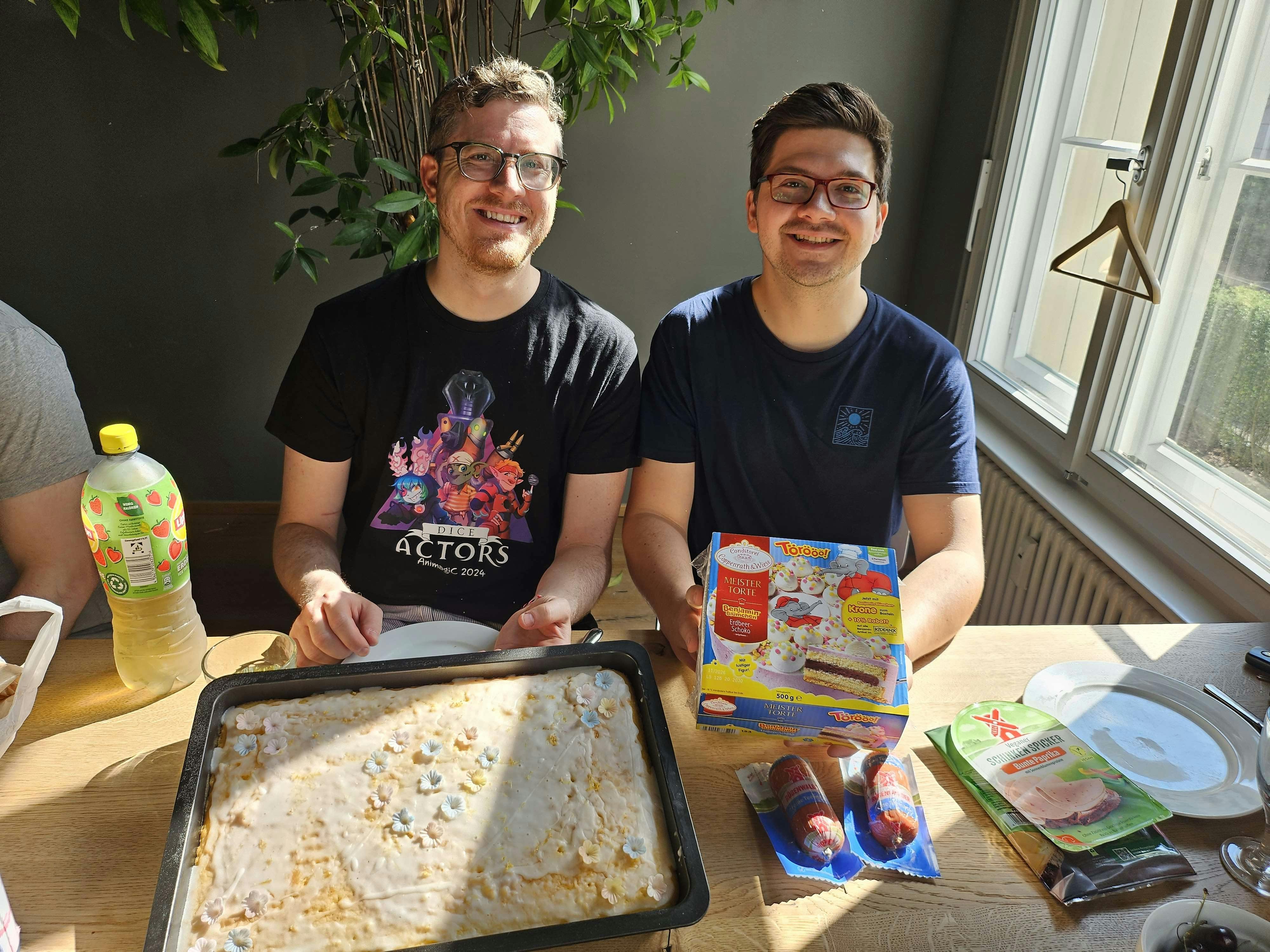 Tim und Patze sitzen mit Zitronenblechkuchen und Benjamin Blümchen-Torte am Frühstückstisch und grinsen.