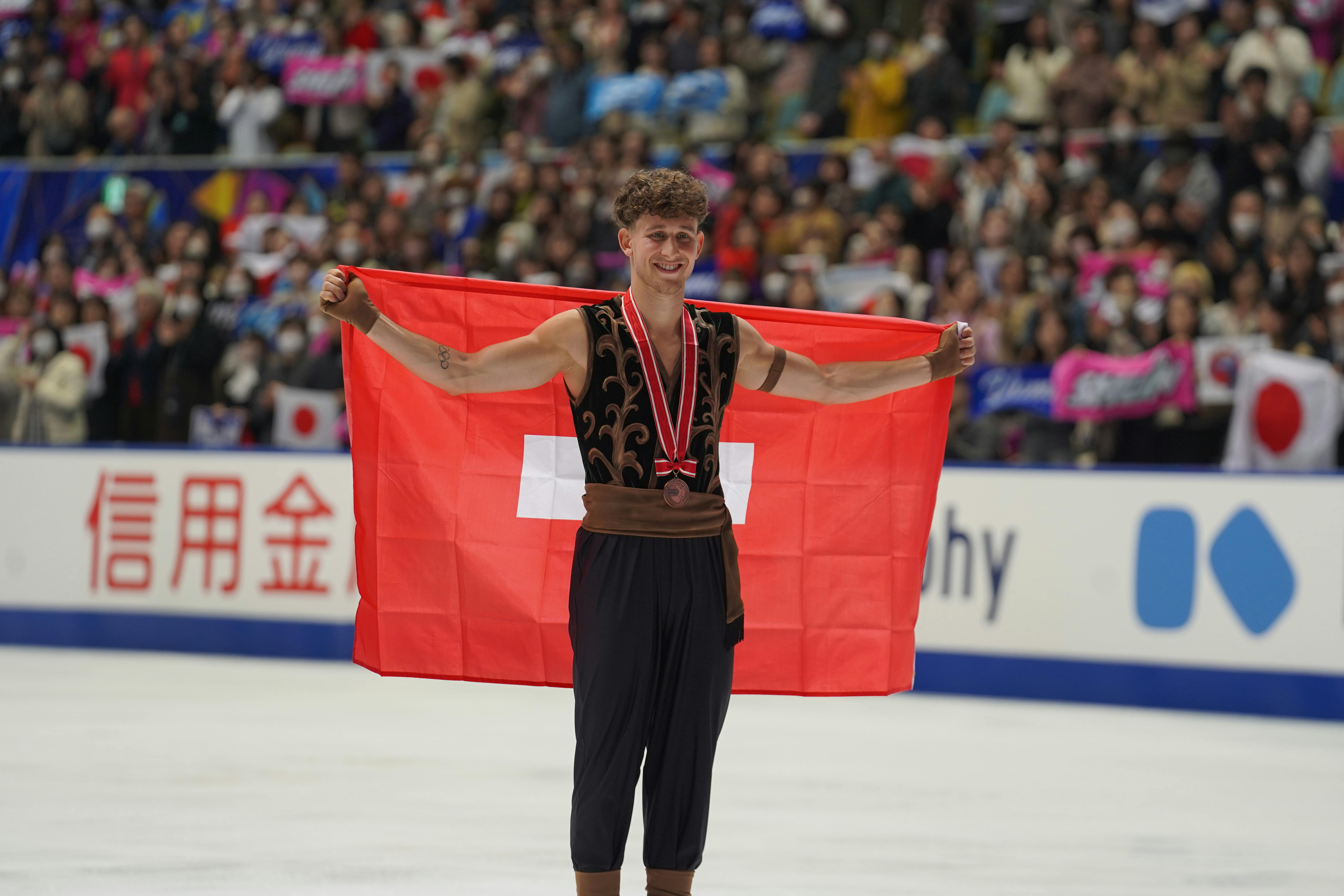 Eiskunstläufer Lukas Britschgi mit der Bronzemedaille und der Schweizer Fahne bei der NHK Trophy