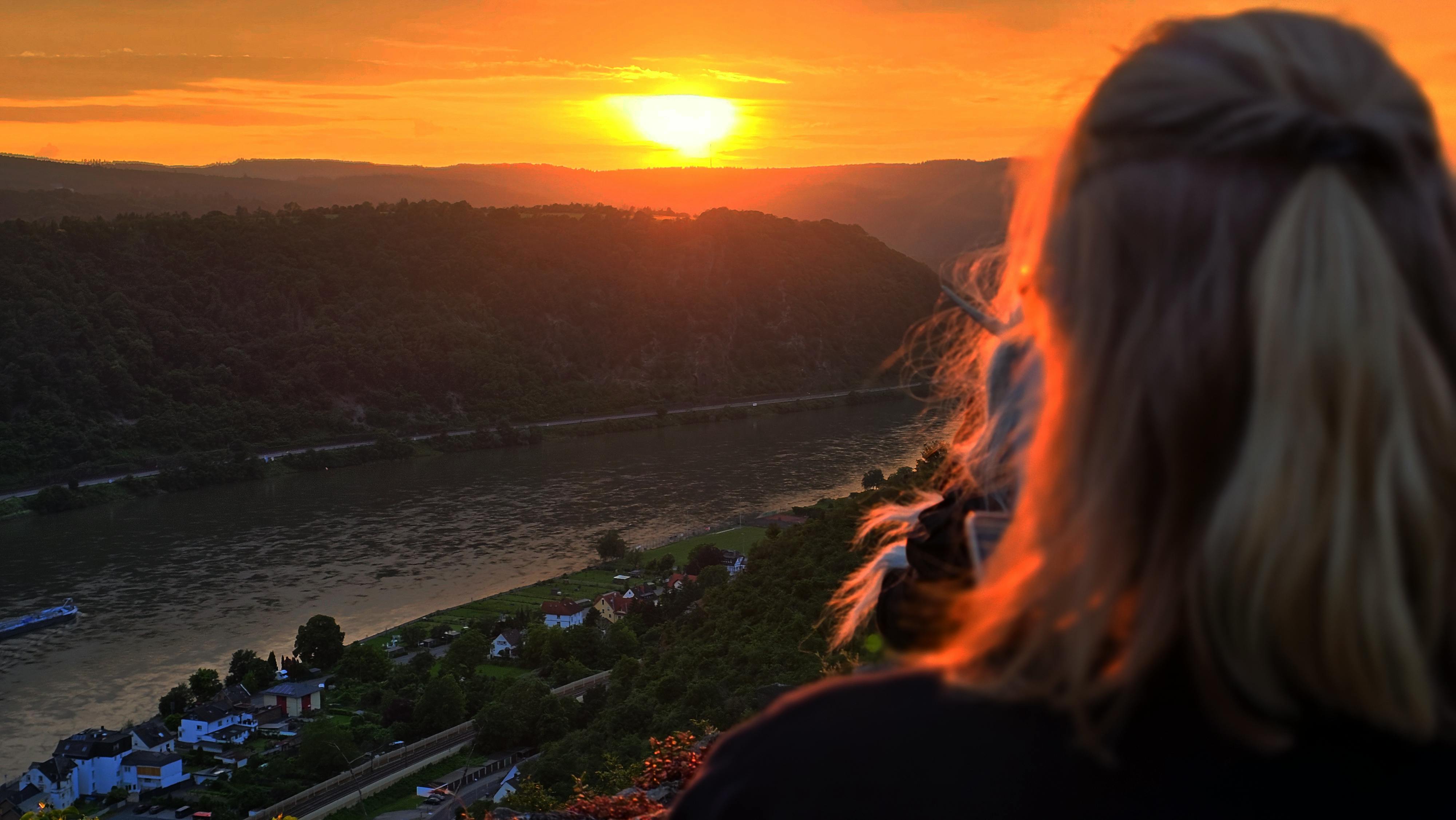 Der Blick von der Burg über den Rein. Im Hintergrund Berge und der Sonnenuntergang.