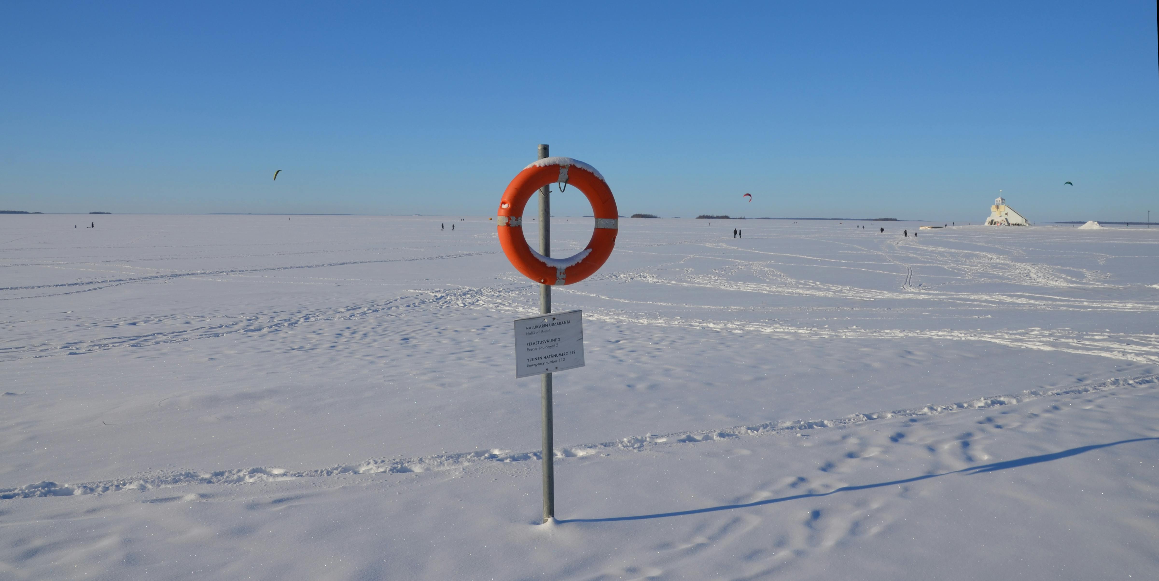 Weiße, ebene Schneefläche bis zum Horizont, Gestell mit orangem Rettungsring