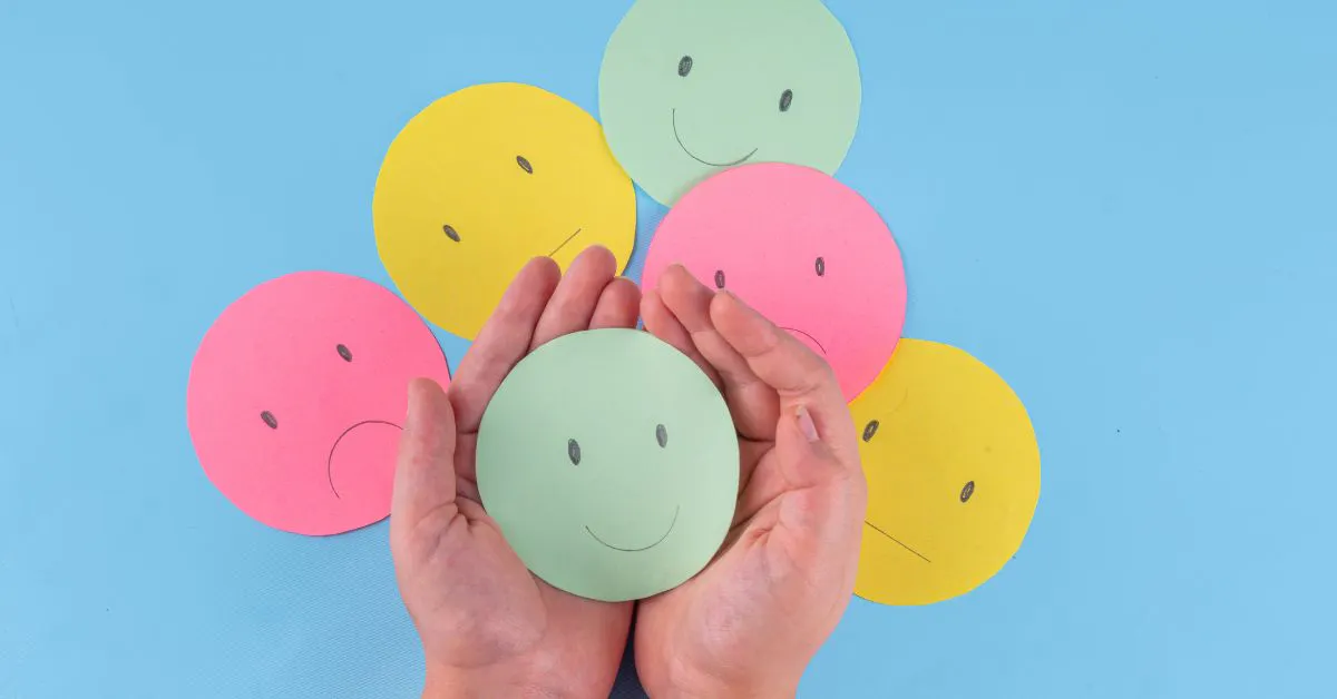Verschiedene Smileys auf einem Tisch, zwei Hände halten einen fröhlichen Smiley