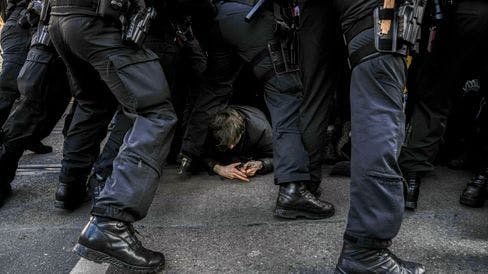 Demonstrant am Boden, überall Polizist:innen, von denen nur Beine, Stiefel und die Gürtel mit Waffen etc. zu sehen sind