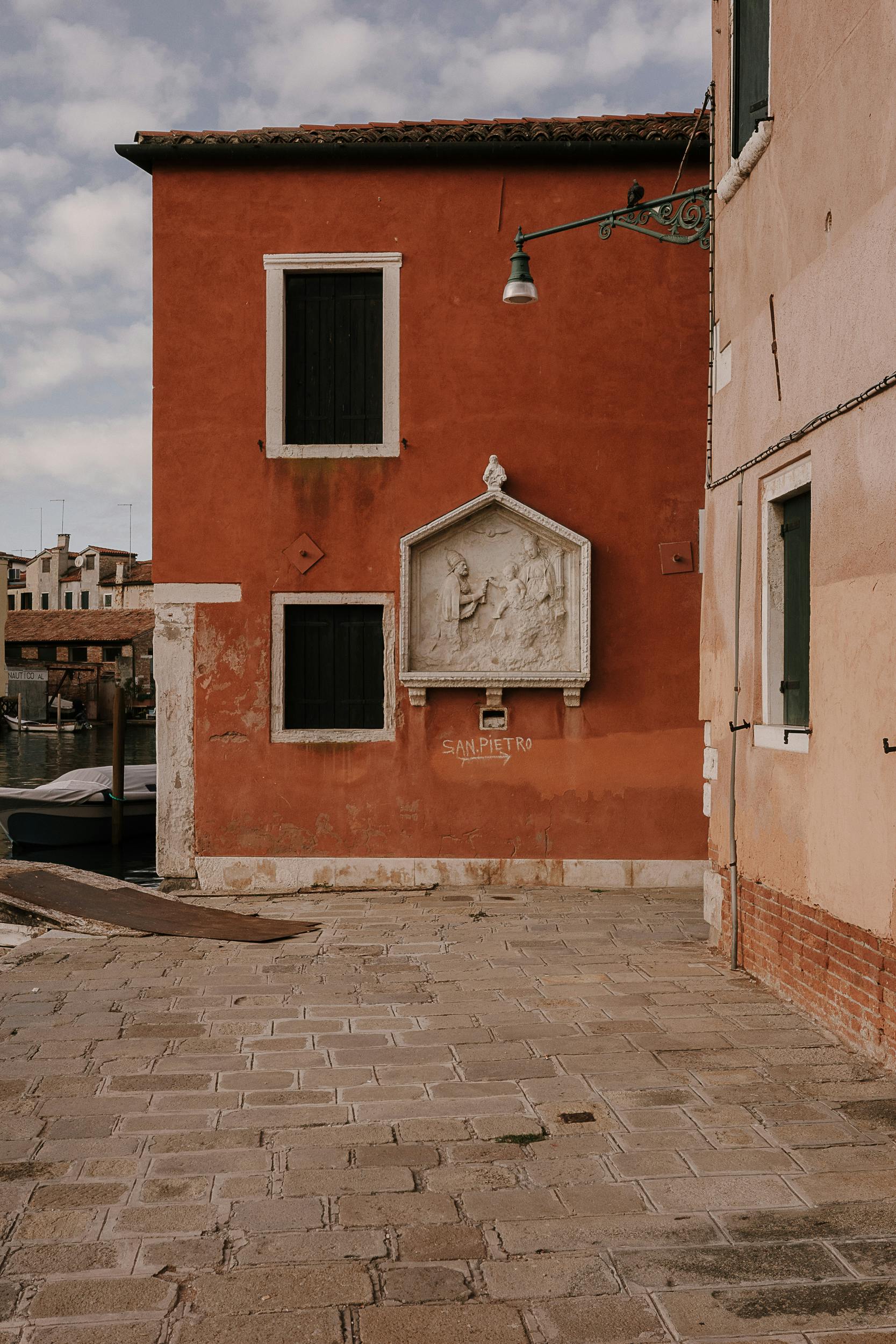 Eine Hauswand in Venedig mit einer Heiligendarstellung aus Stein. Mit Kreide steht "St. Pietro" angeschrieben, darunter ein Pfeil nach rechts.