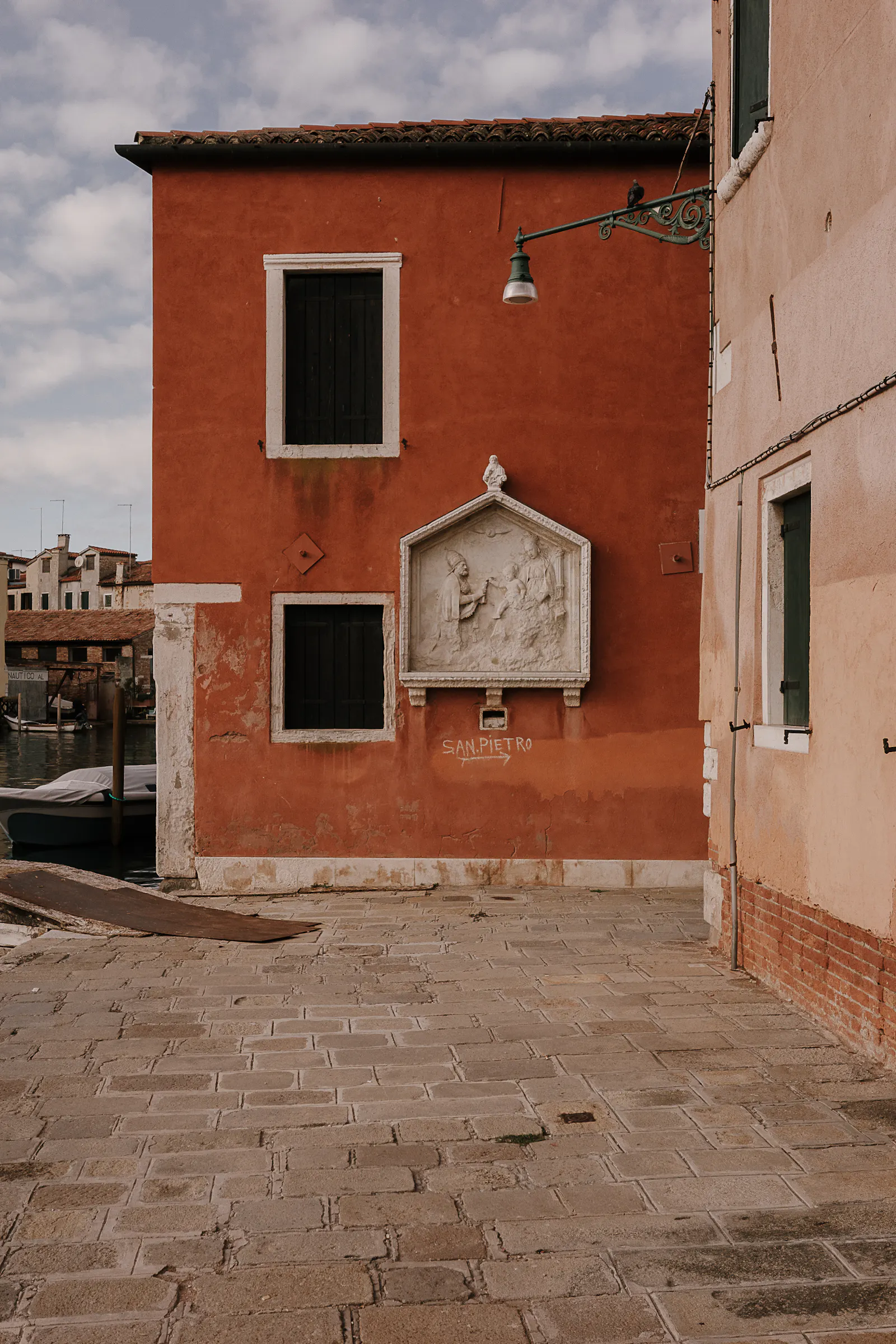 Eine Hauswand in Venedig mit einer Heiligendarstellung aus Stein. Mit Kreide steht "St. Pietro" angeschrieben, darunter ein Pfeil nach rechts.