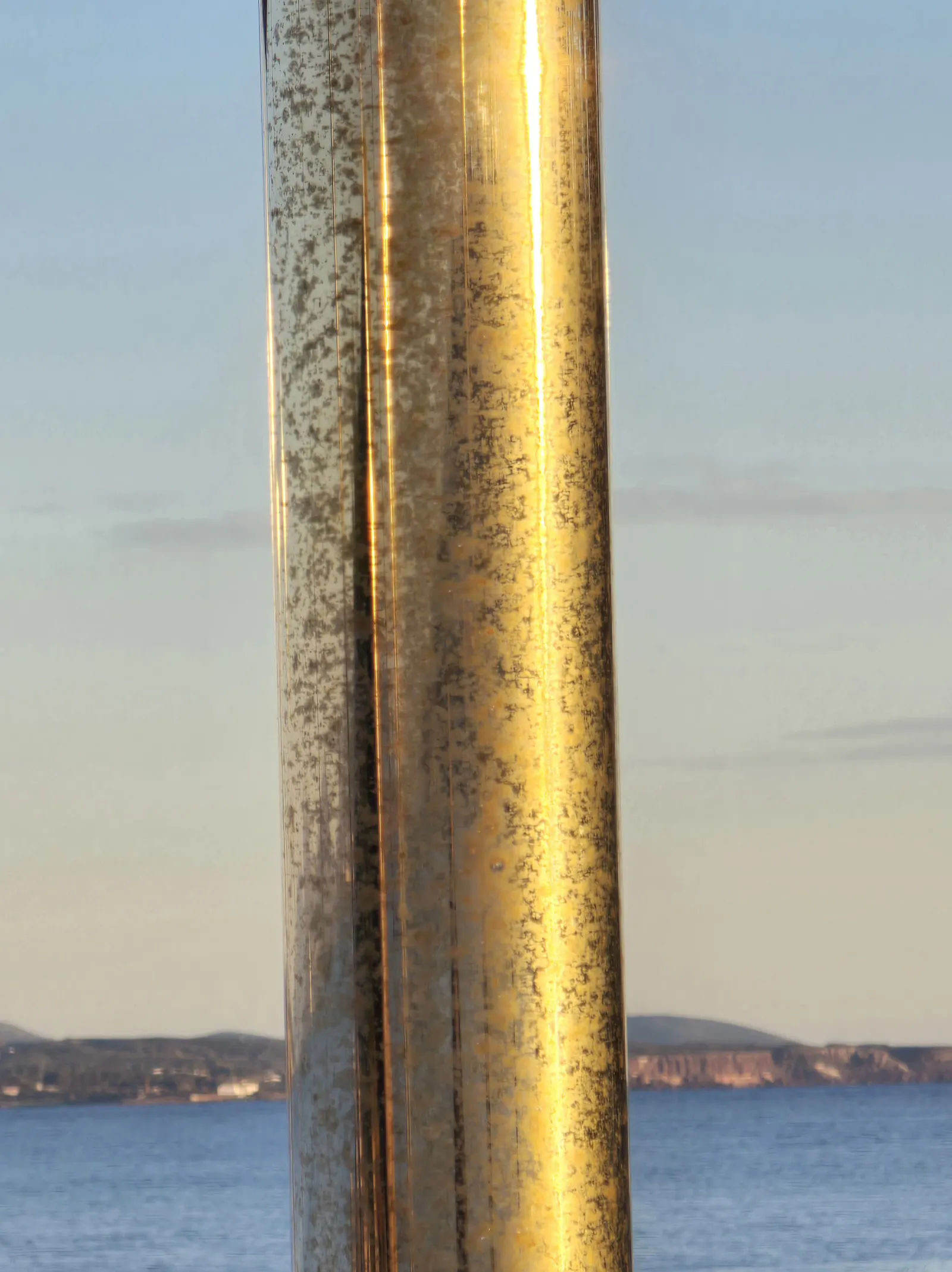 Von der Sonne golden angestrahlte Metallstange vor Meer