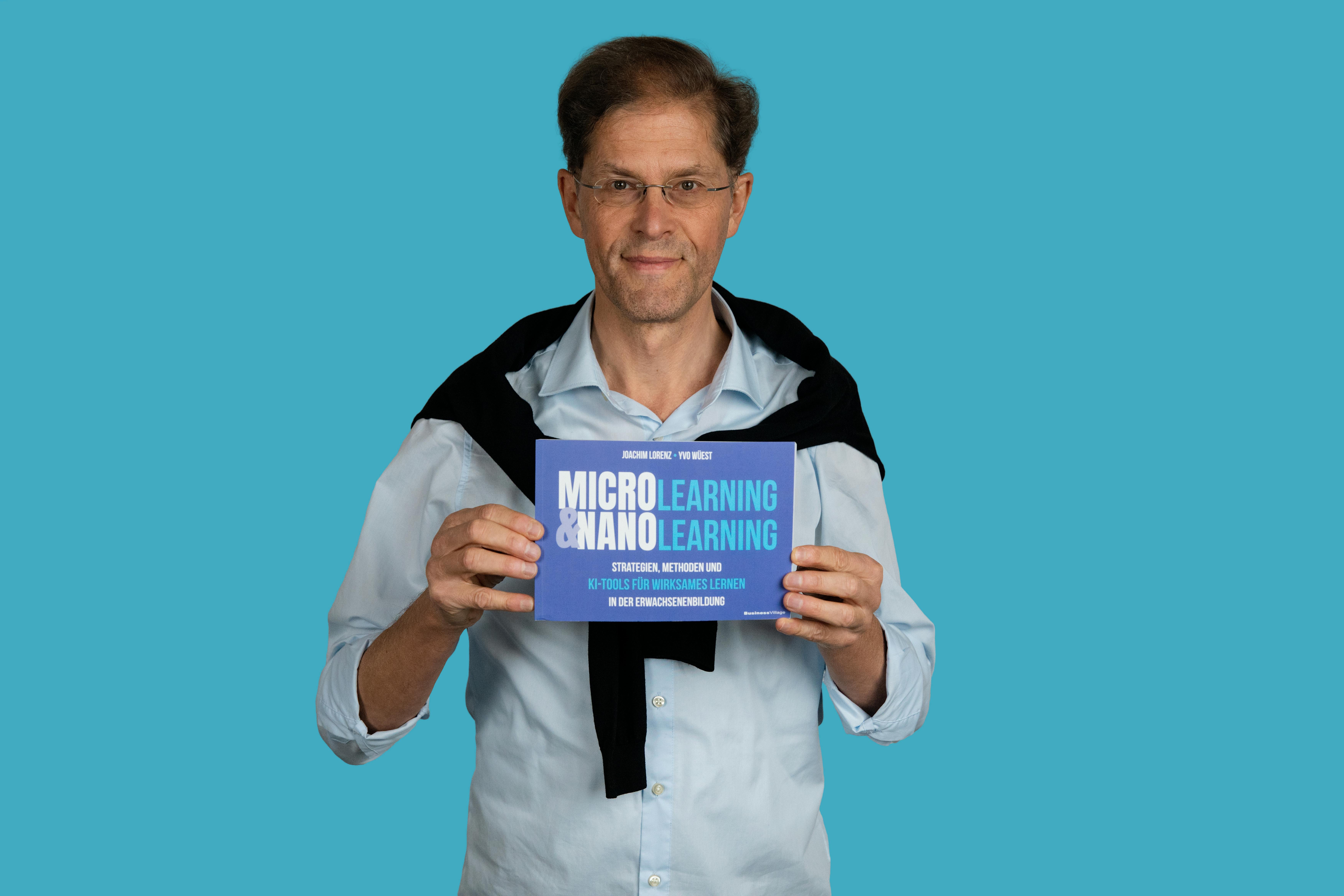 Yvo Wüest mit dem neuen Fachbuch "Microlearning und Nanolearning" (2025) in der Hand vor hellblauem Hintergrund.