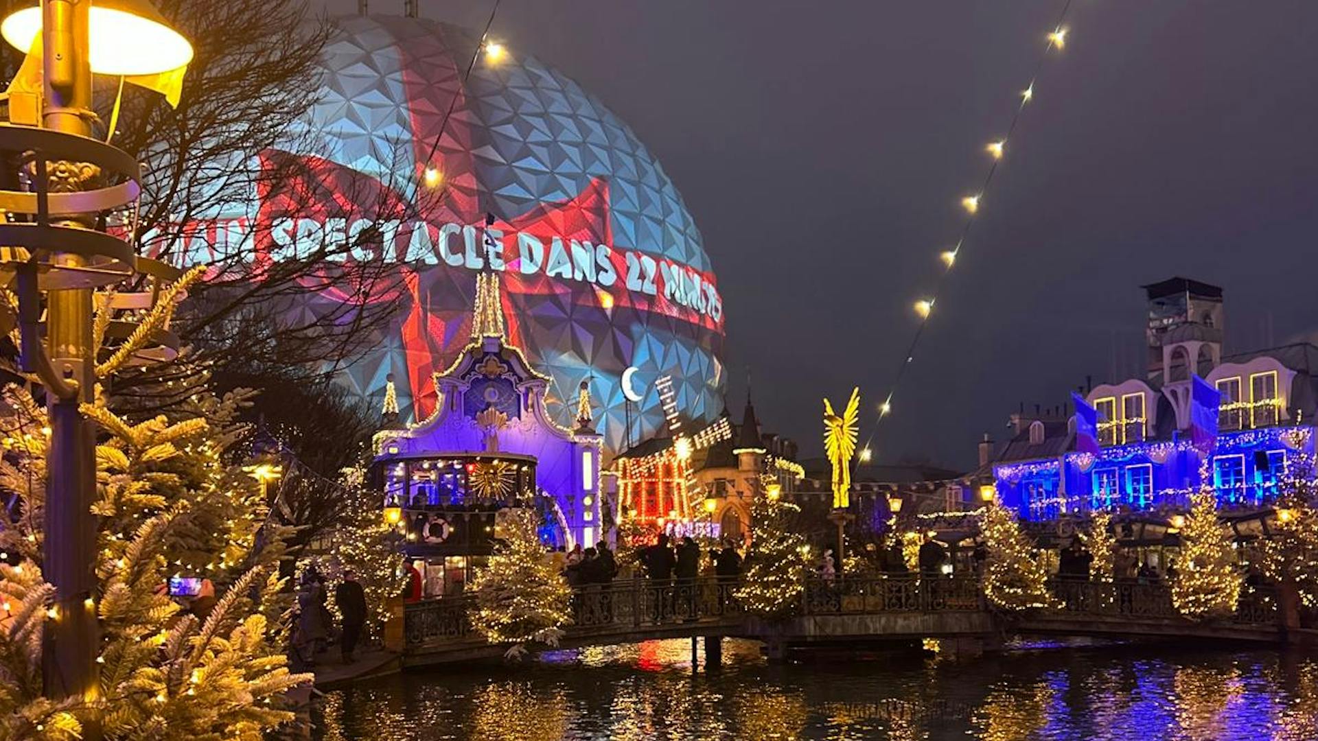 Winterlich dekorierte Häuserfronten an einem See und eine gigantische Kugel, die wie ein Weihnachtsgeschenk beleuchtet ist