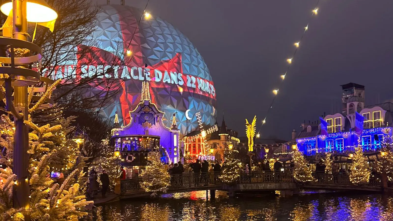 Winterlich dekorierte Häuserfronten an einem See und eine gigantische Kugel, die wie ein Weihnachtsgeschenk beleuchtet ist