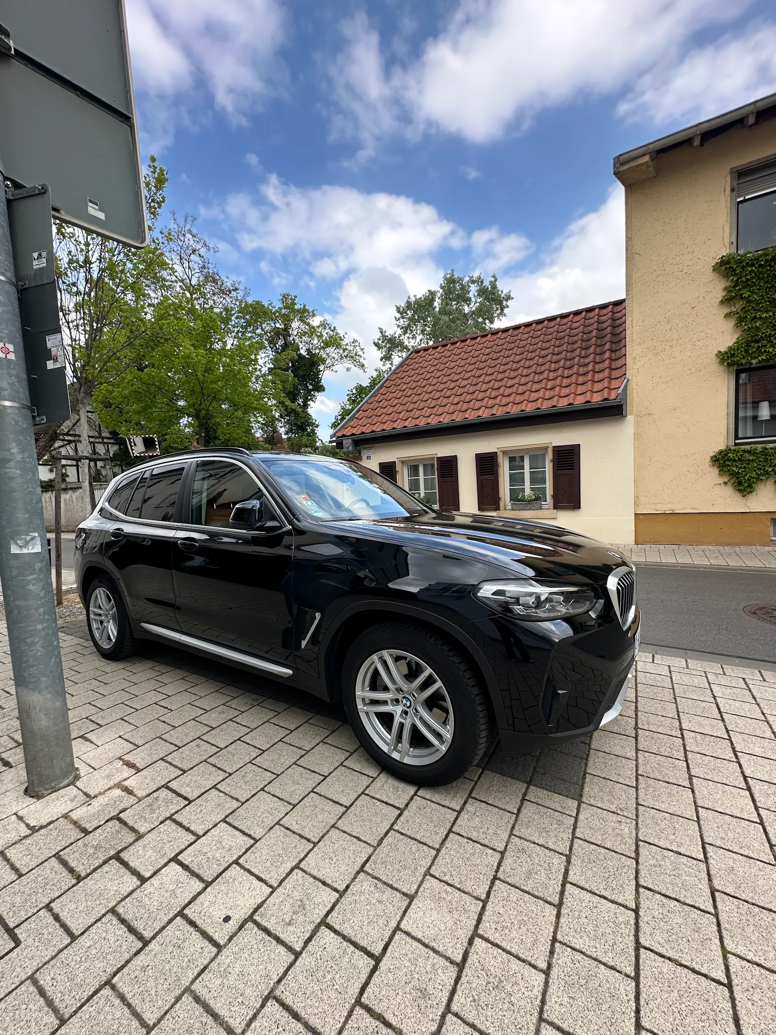 Großer schwarzer SUV, im Hintergrund ein mittelalterliches Haus, das kleiner ist als das geparkte Auto.