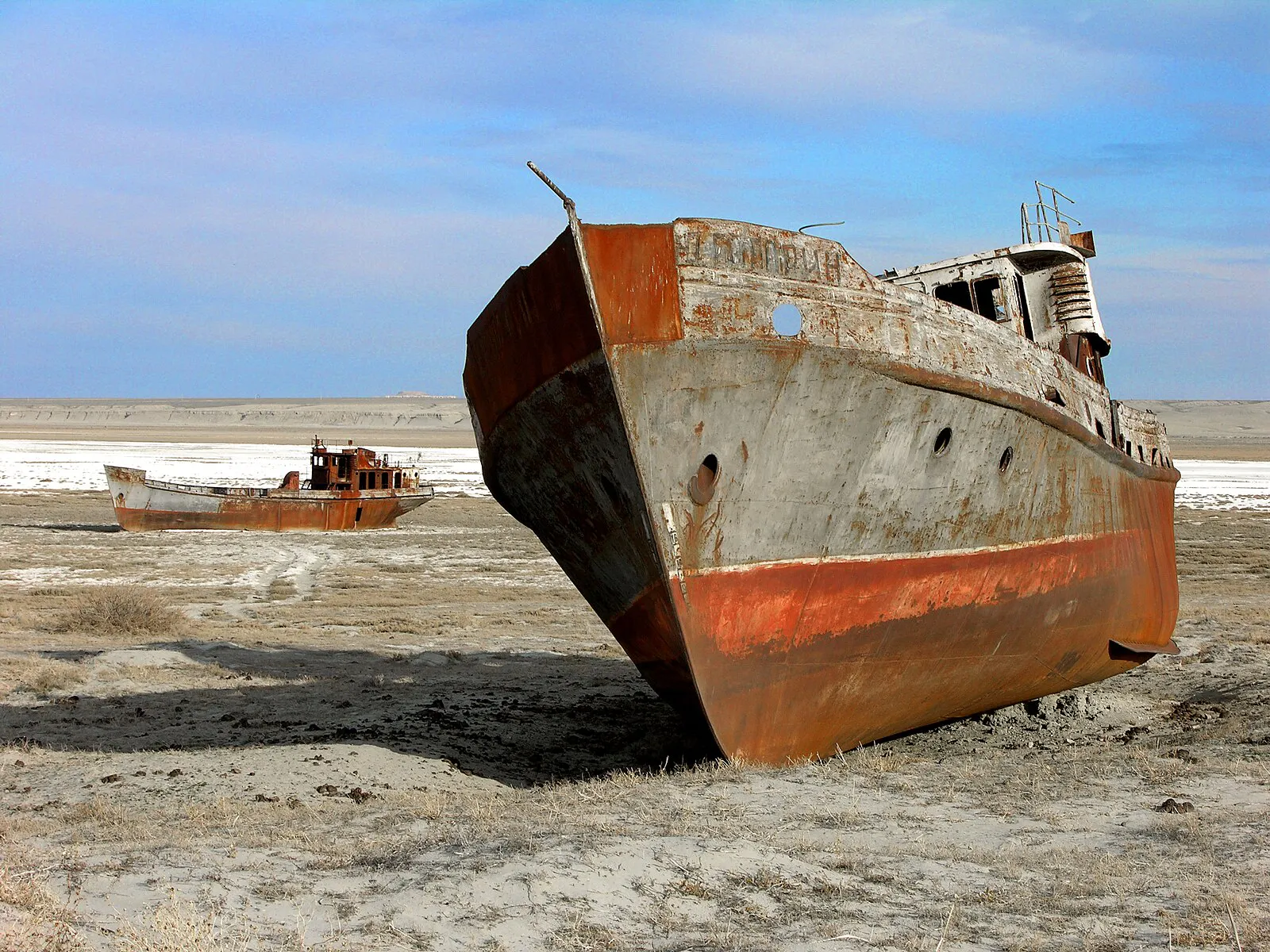 Das Foto zeigt ein verrostetes Boot, das auf ausgetrocknetem Boden liegt.