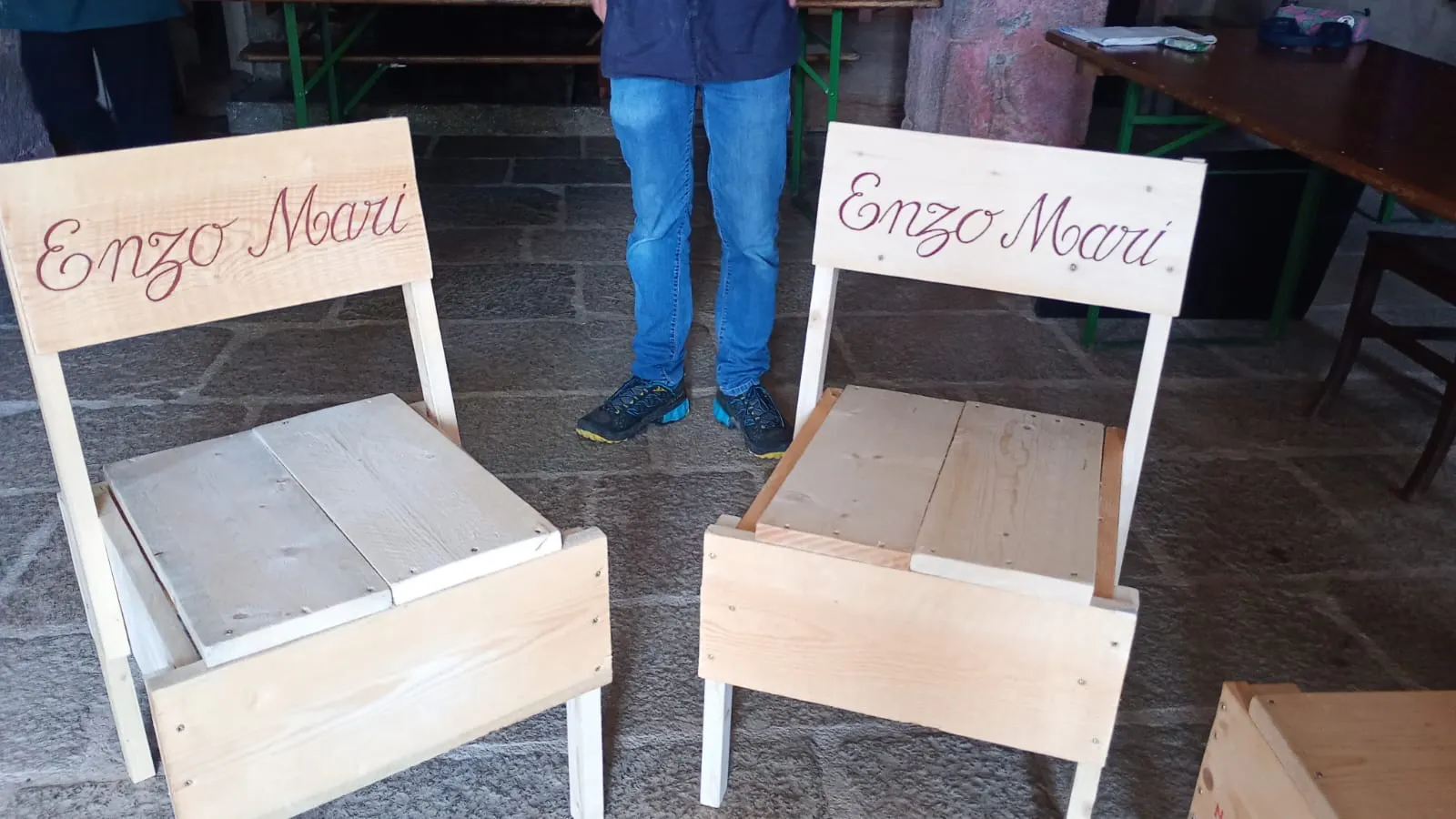 Immagine di sedie in legno di abete, su pavimento in pietra. Le sedie hanno scritte "Enzo Mari" un bella calligrafia