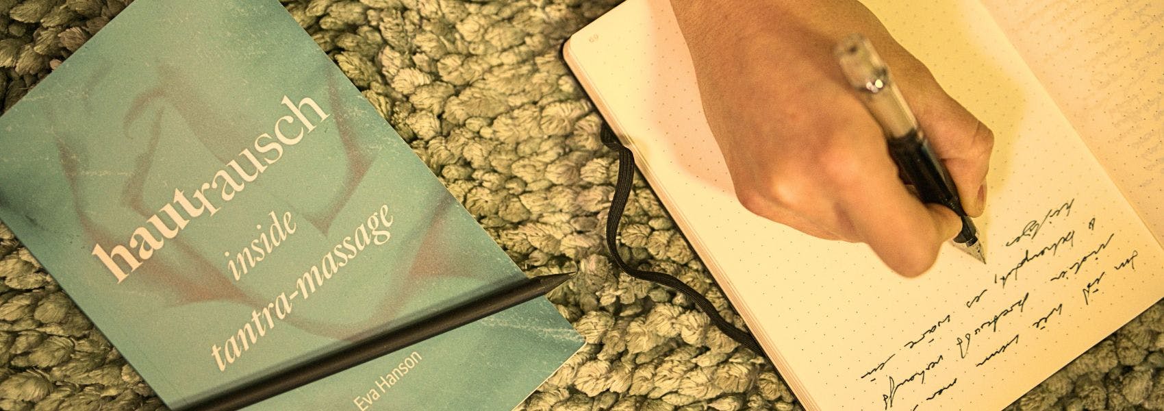 Hautrausch-Inside Tantra-Massage liegt mit einem schwarzem Notizbuch, in dem Eva gerade schreibt
