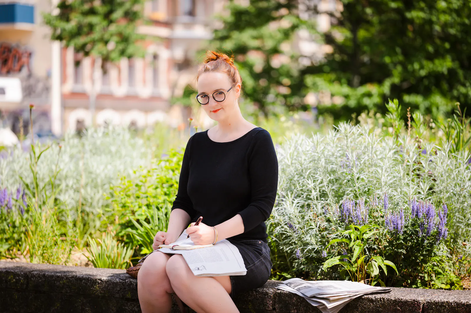 Insa van den Berg, Frau mit roten Haaren und Brille, sitzt im Park und macht sich Notizen.