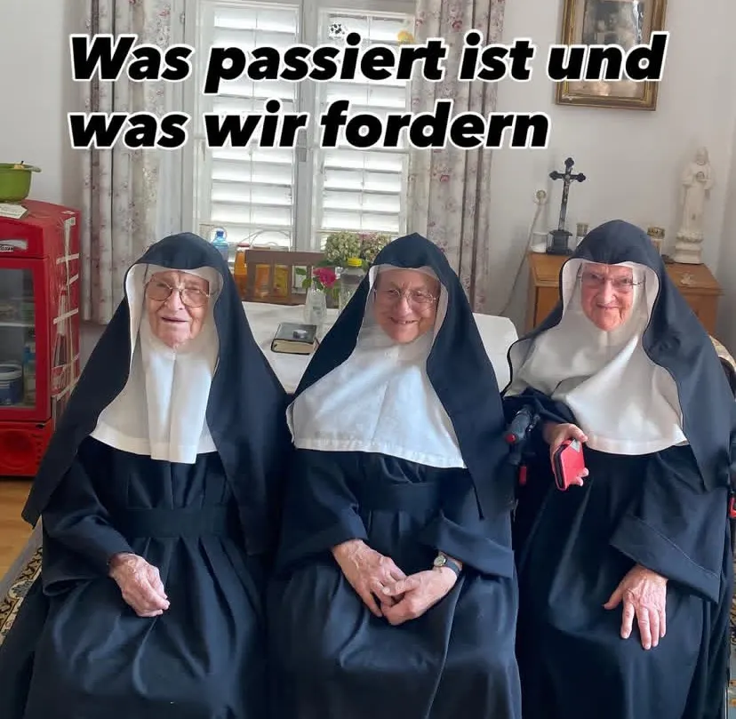 Diese Foto zeigt die drei Nonnen Regina, Rita und Bernadette in traditioneller schwarzer Ordenstracht mit weißem Schleier sitzen nebeneinander in einem Raum. Hinter ihnen steht ein Tisch mit Blumen, Büchern und religiösen Gegenständen.