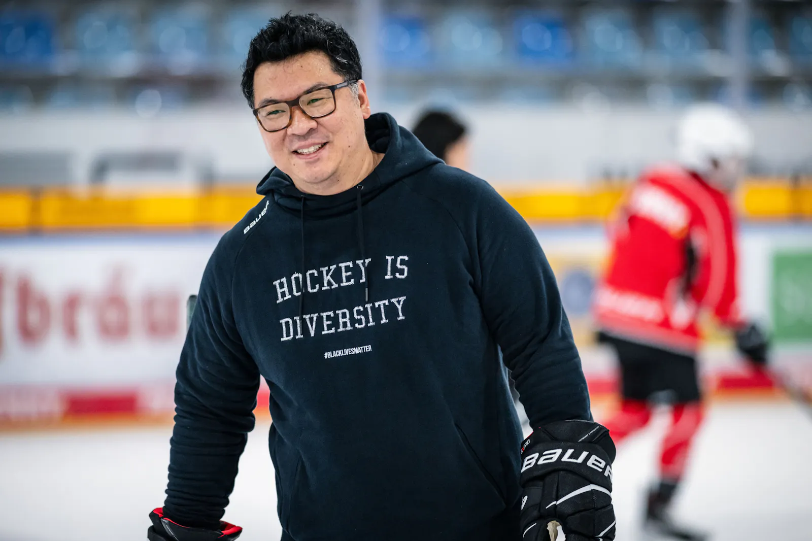 Martin Hyun steht auf dem Eis und lächelt. Er trägt einen schwarzen Hoodie mit der Aufschrift "Hockey is Diversity".