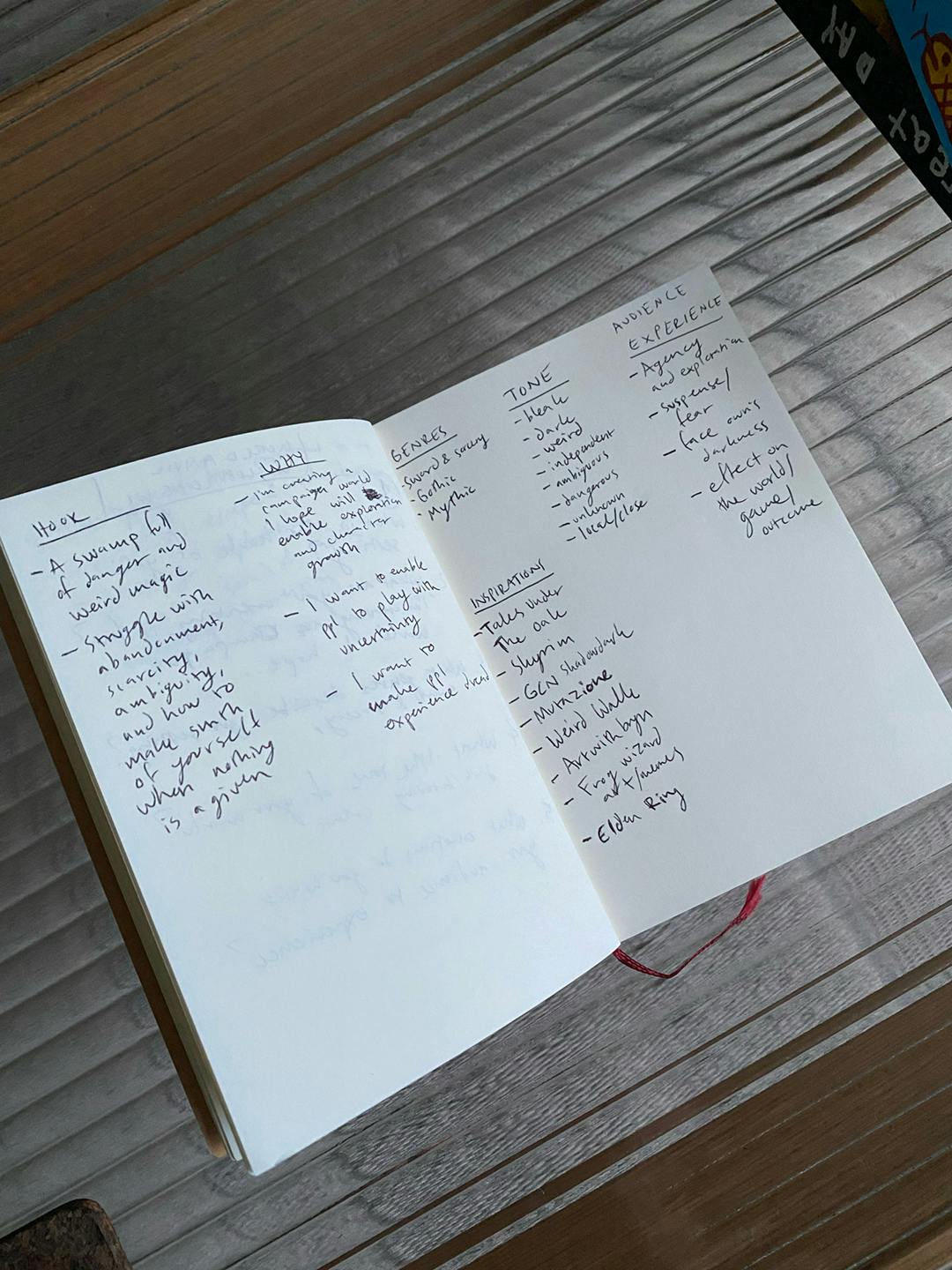 Photo of a small notebook on a glass table. It is filled with handwritten notes corresponding to Anders's brain dump for starting his worldbuilding project.