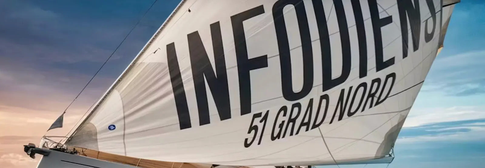 Bild eines Segelbootes in voller Fahrt. Auf dem Segel steht "Infodienst - 51° Nord"