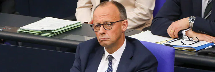 Friedrich Merz schaut mit nach unten zeigenden Mundwinkeln in die Luft. Er sitzt auf seinem Platz im Parlament.