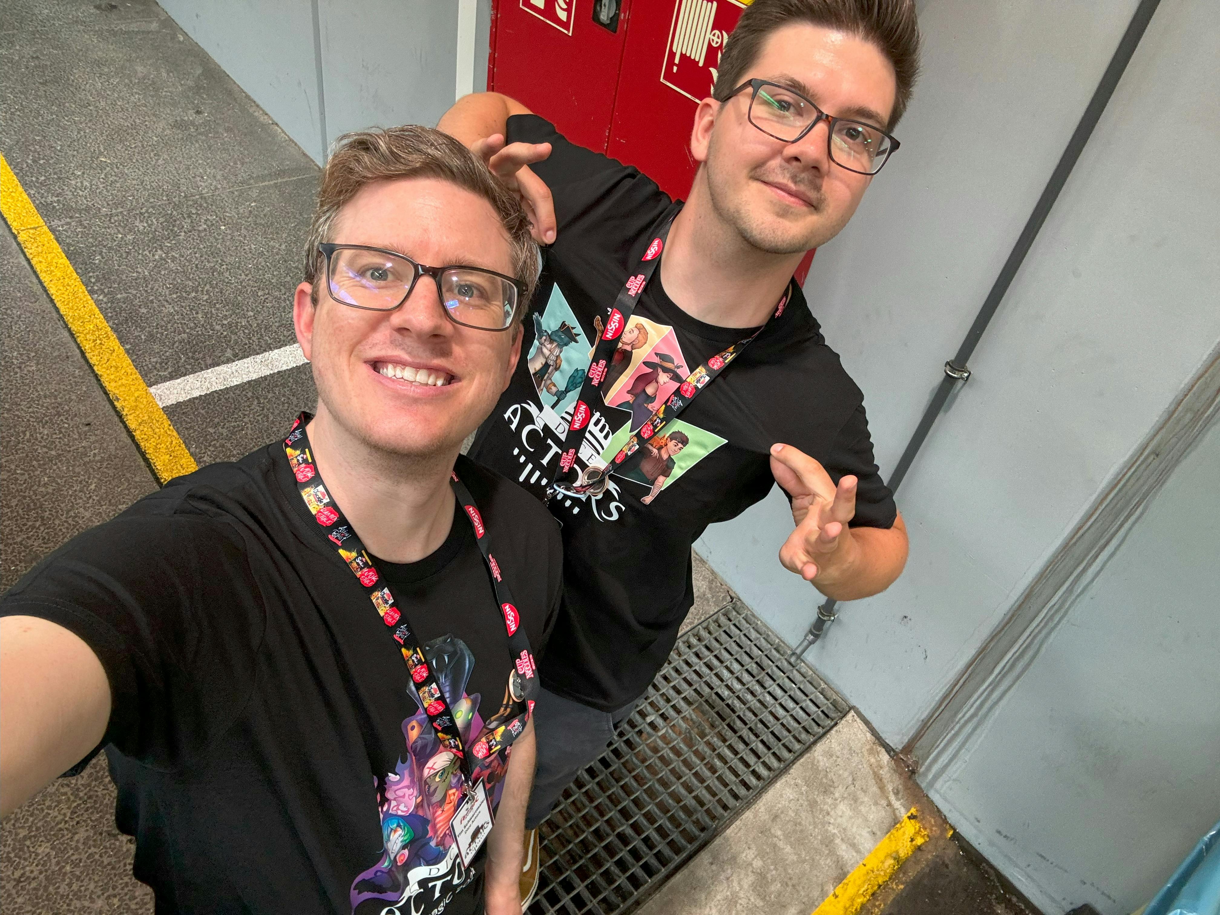 Tim und Patze stehen in einem Flur auf der AnimagiC und tragen beide voller stolz ein Shirt der Hüter der Obelisken und eines der Bolzenbande.
