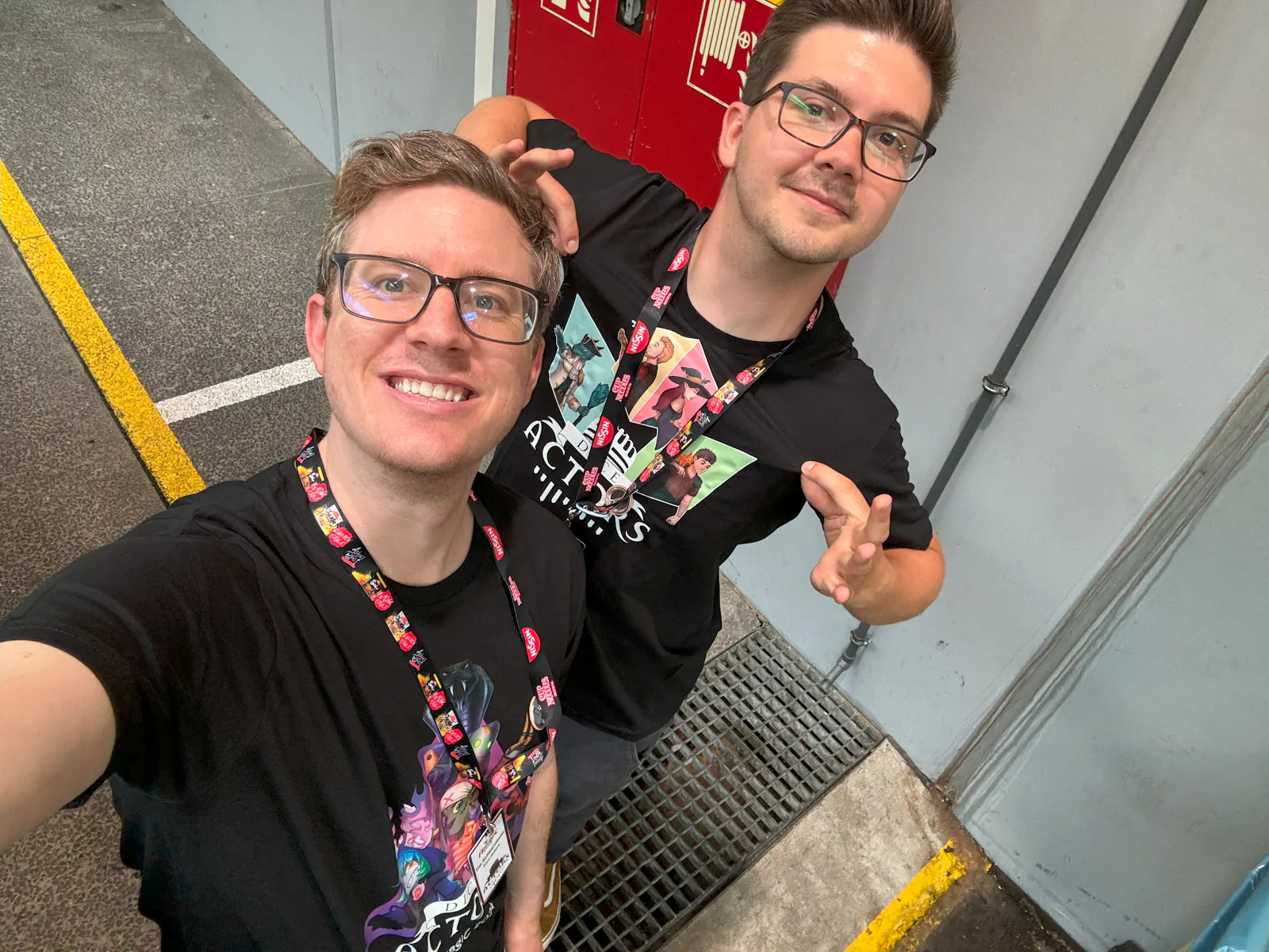 Tim und Patze stehen in einem Flur auf der AnimagiC und tragen beide voller stolz ein Shirt der Hüter der Obelisken und eines der Bolzenbande.