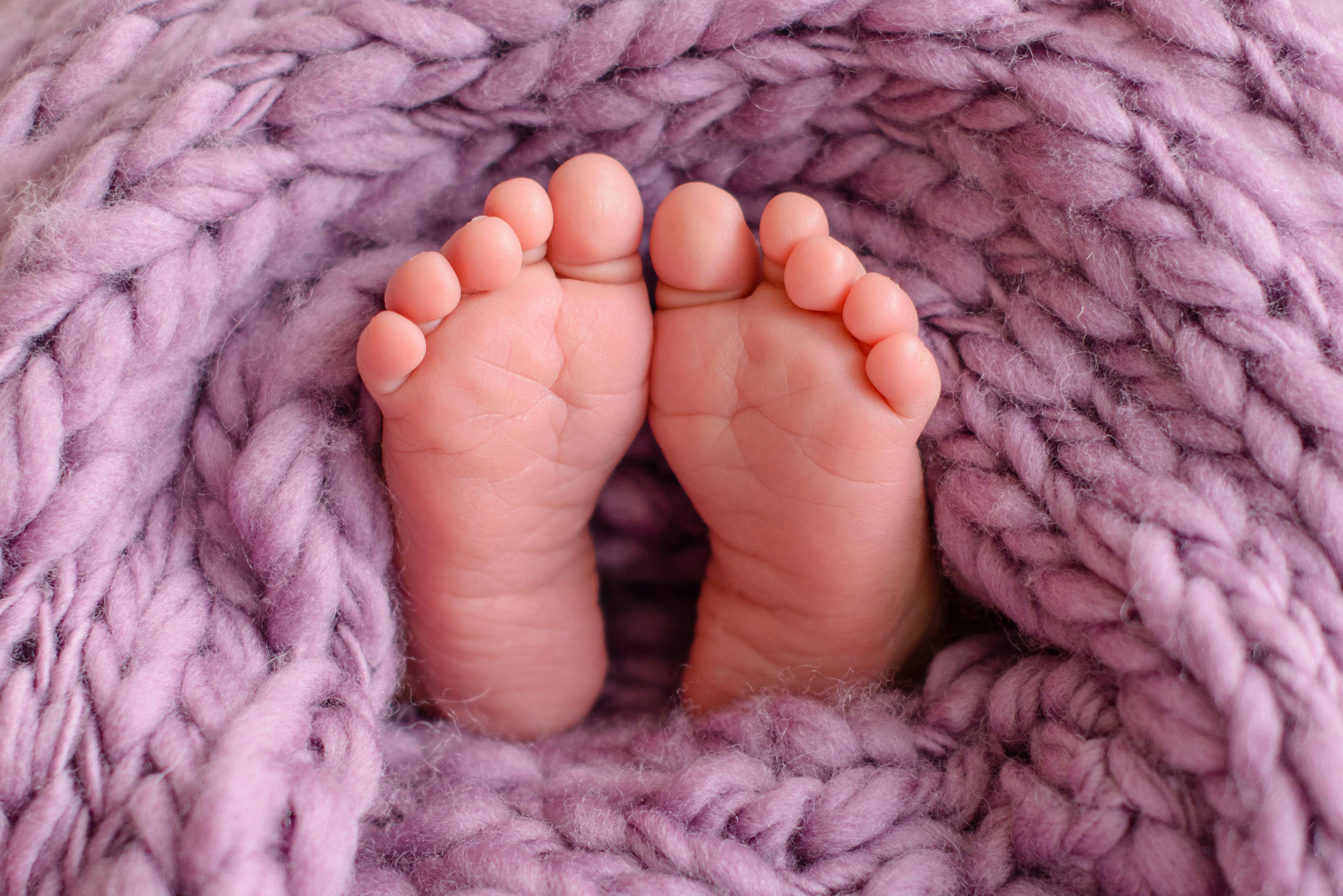 Das Foto zeigt zwei kleine Babyfüße auf einer rosa-lila Strickdecke