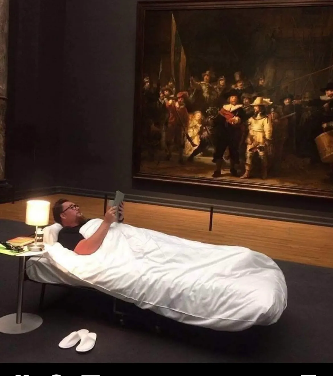 Mensch liegt im Museum mit Buch im Bett vor Gemälde