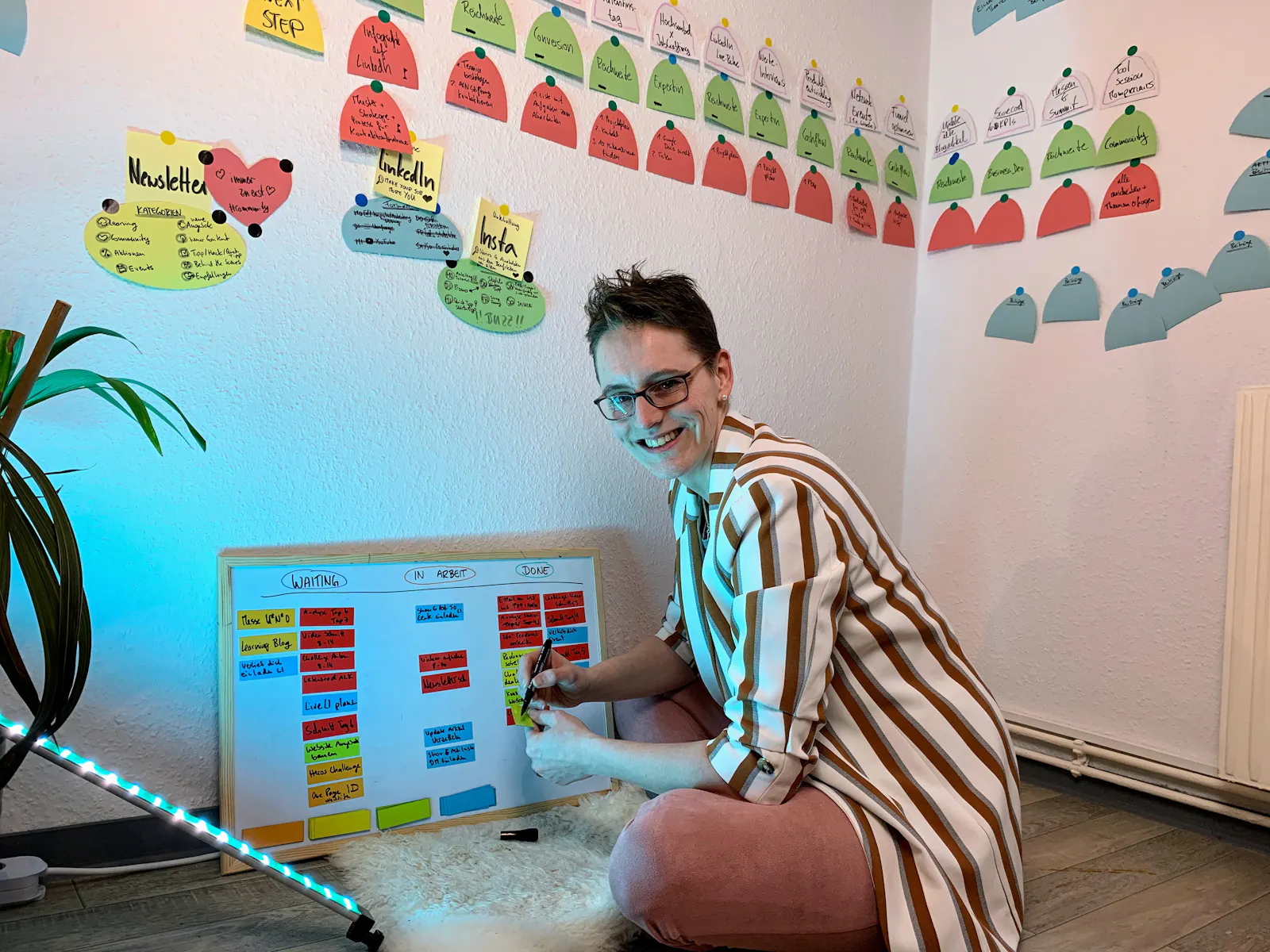 Antonia sitzt auf dem Boden vor einem Whiteboard mit Magnetkarten dran. An die Wand im Hintergrund sind sehr viele Zettel geklebt.