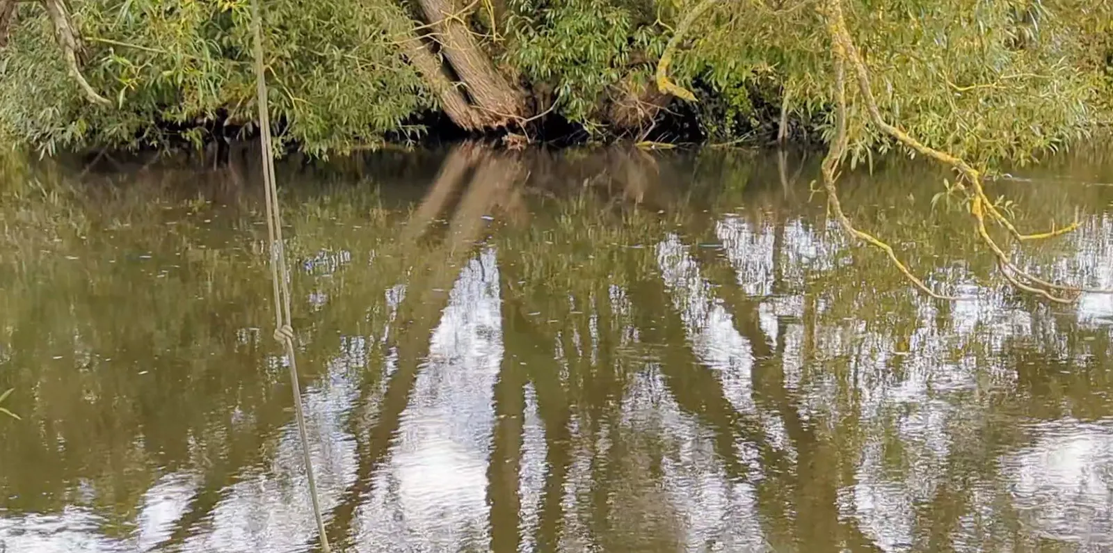 Eine Stelle am Fluss, die ich sehr mag. Im Hintergrund ist die Uferböschung zu sehen. Links hängt ein Seil ins Wasser, an dem man sich beim Schwimmen festhalten kann.
