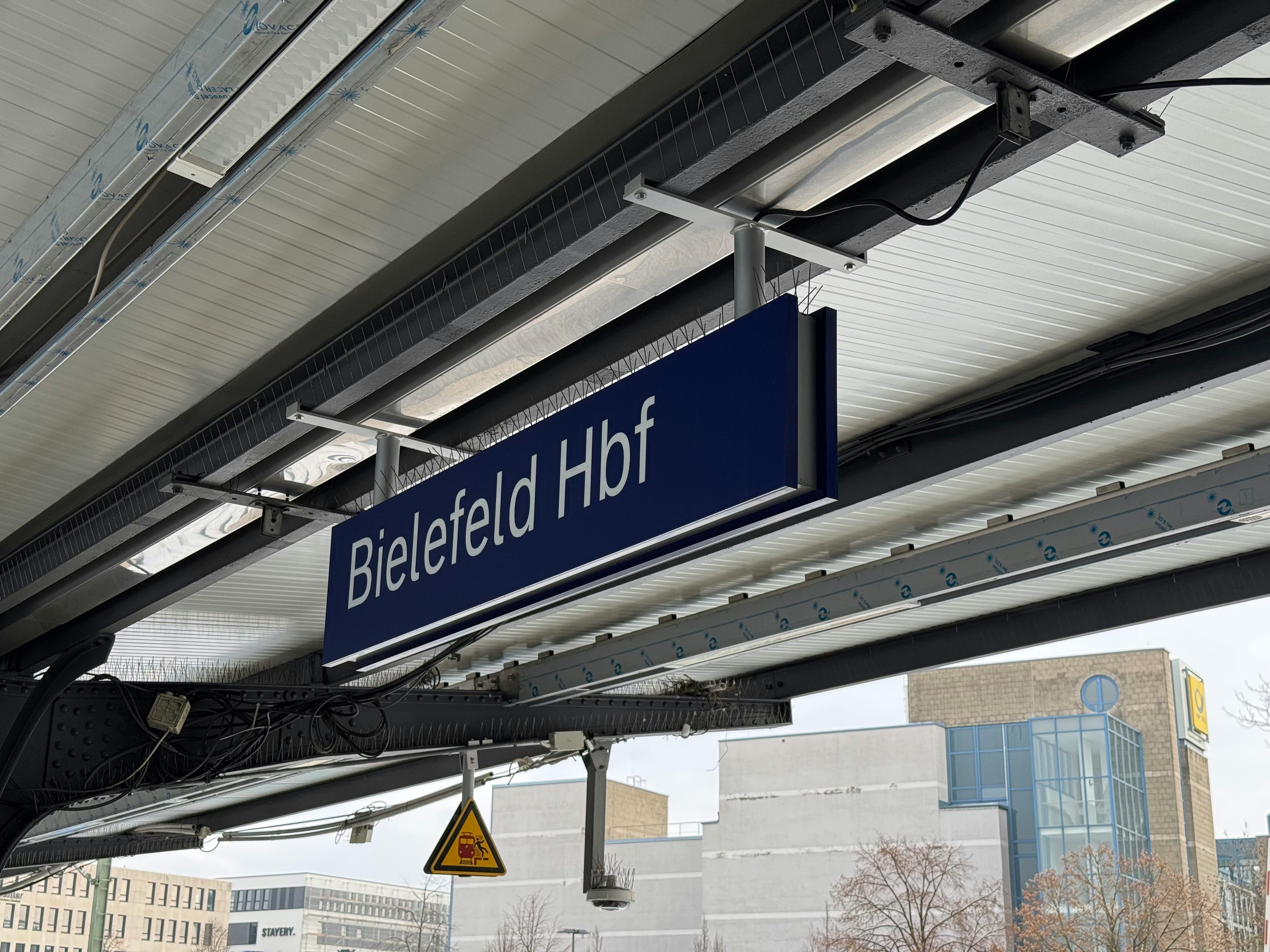 Das Bild zeigt das Dach eines Bahnhofs und eine Tafel mit der Aufschrift "Bielefeld Hbf".