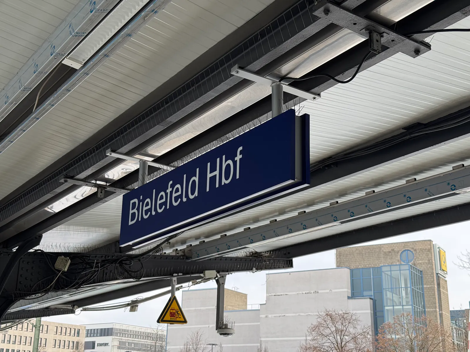 Das Bild zeigt das Dach eines Bahnhofs und eine Tafel mit der Aufschrift "Bielefeld Hbf".