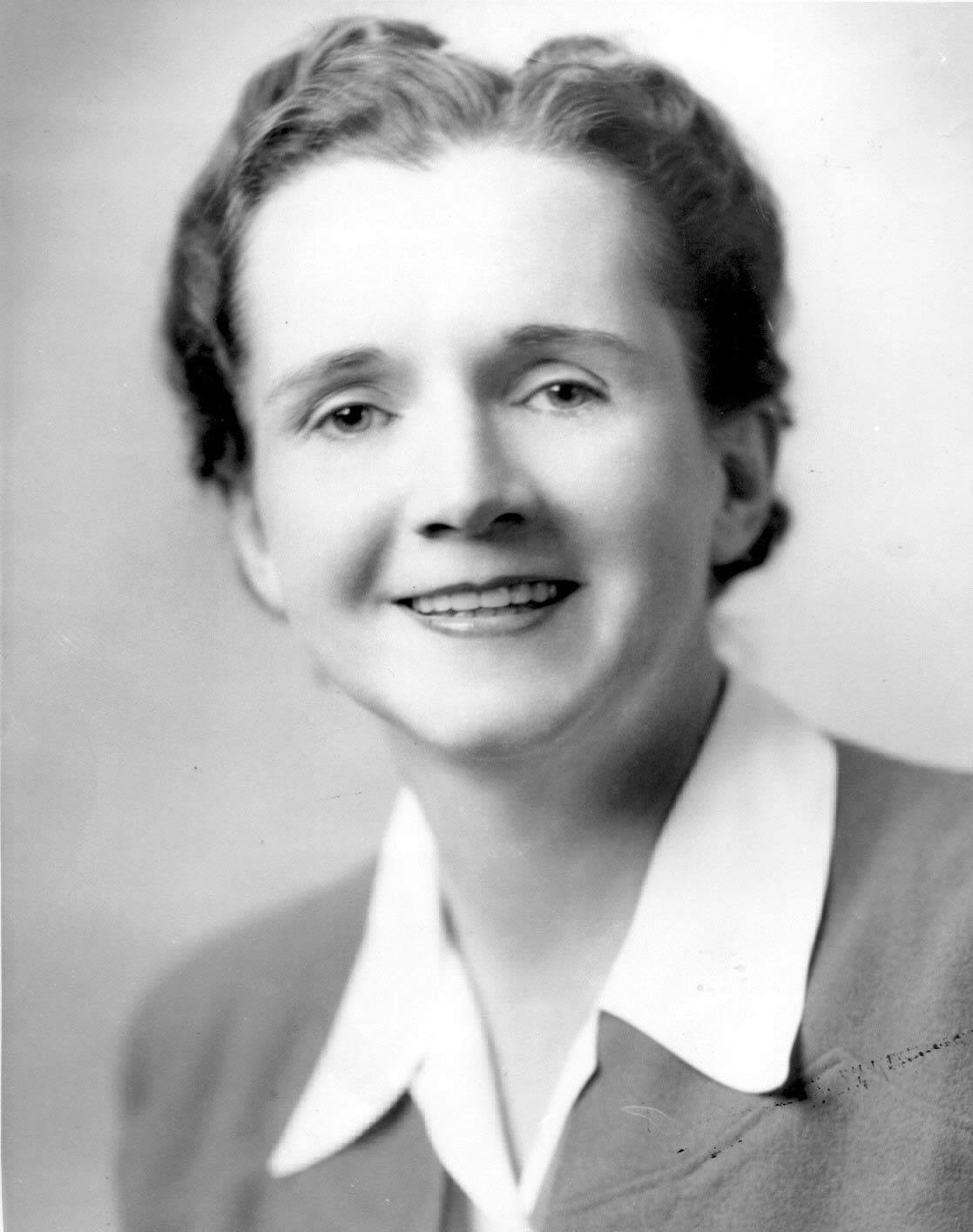 Ein altes Schwarz-Weiß-Foto einer jungen Frau mit braunen, kurzen Haaren und einem weißen Blusenkragen, die in die Kamera lächelt.