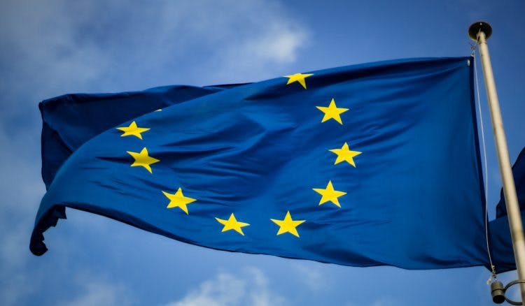 Eine blaue Europafahne mit gelben Sternen weht im Wind vor blauem Himmel.