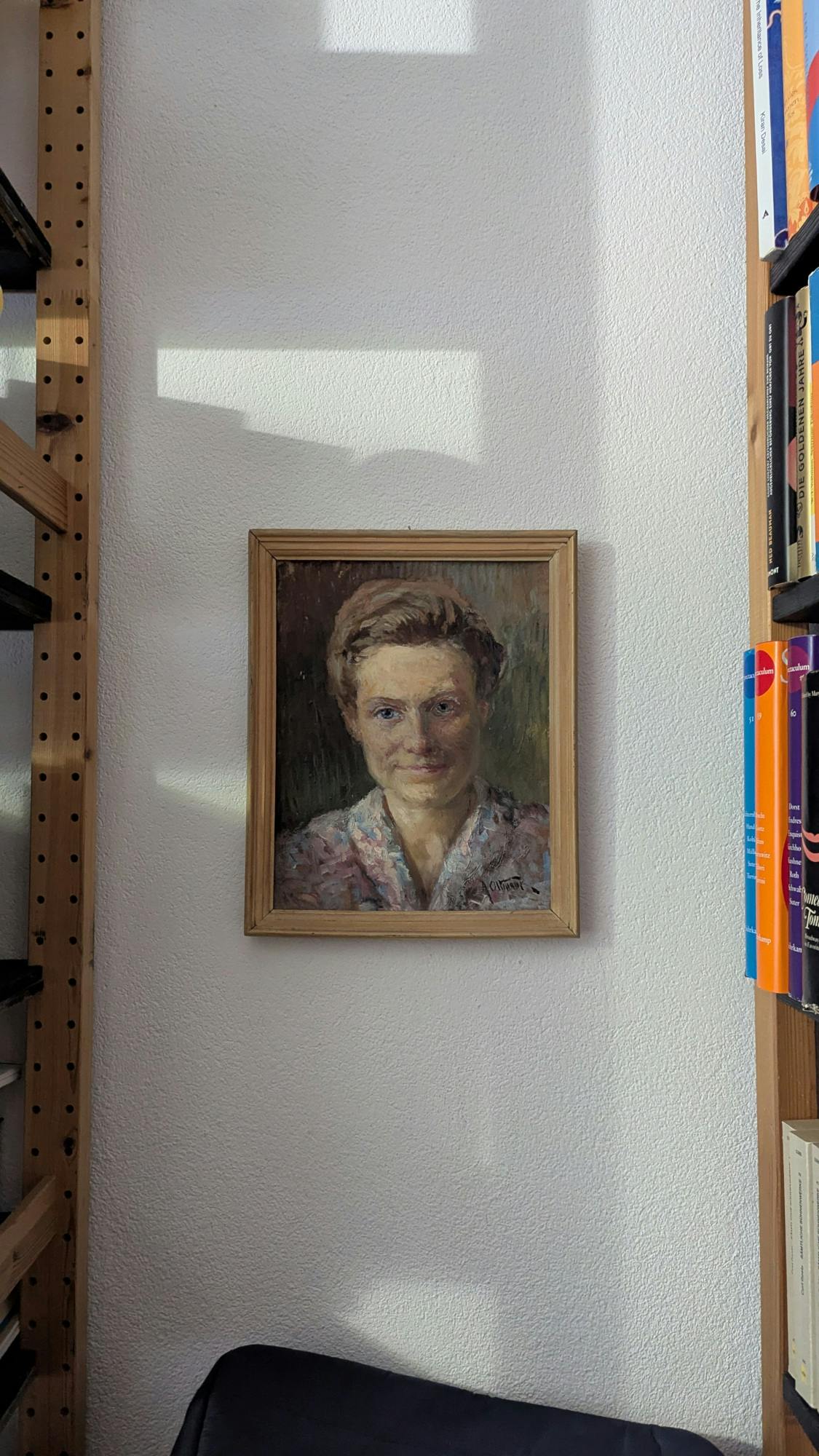 Kleines Öl-Porträt einer jungen Frau mit blauen Augen und weichem Gesicht in einem Rahmen aus Holz an einer weißen Wand zwischen Bücherregalen.