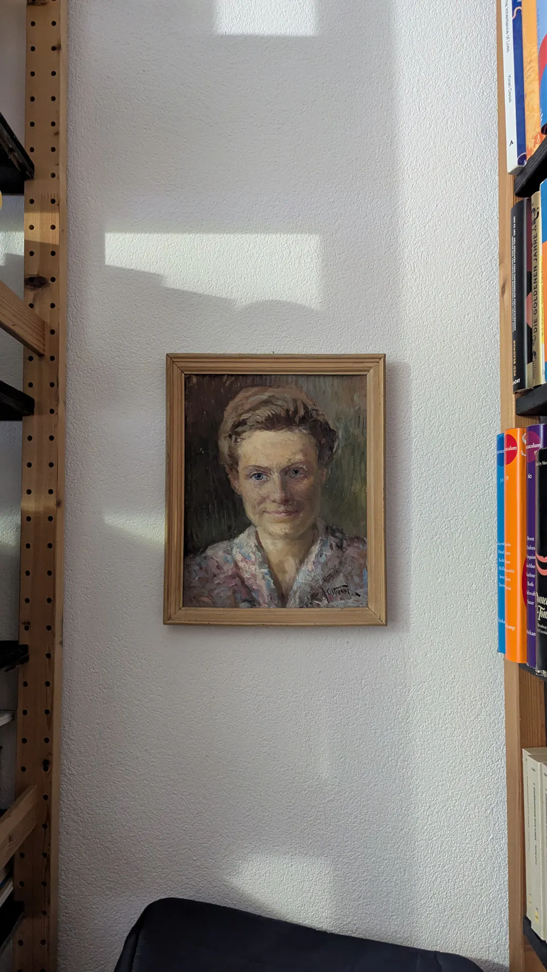 Kleines Öl-Porträt einer jungen Frau mit blauen Augen und weichem Gesicht in einem Rahmen aus Holz an einer weißen Wand zwischen Bücherregalen.