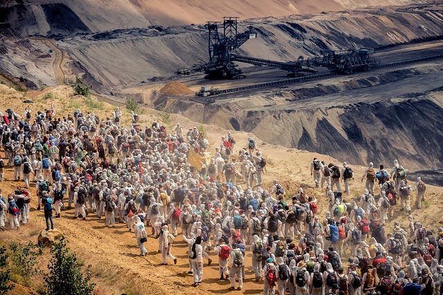 Bild einer Massenaktion von Ende Gelände, Tagebau mit einem Kohlebagger im Hintergrund, Menschen in weißen Maleranzügen stürmen den Tagebau