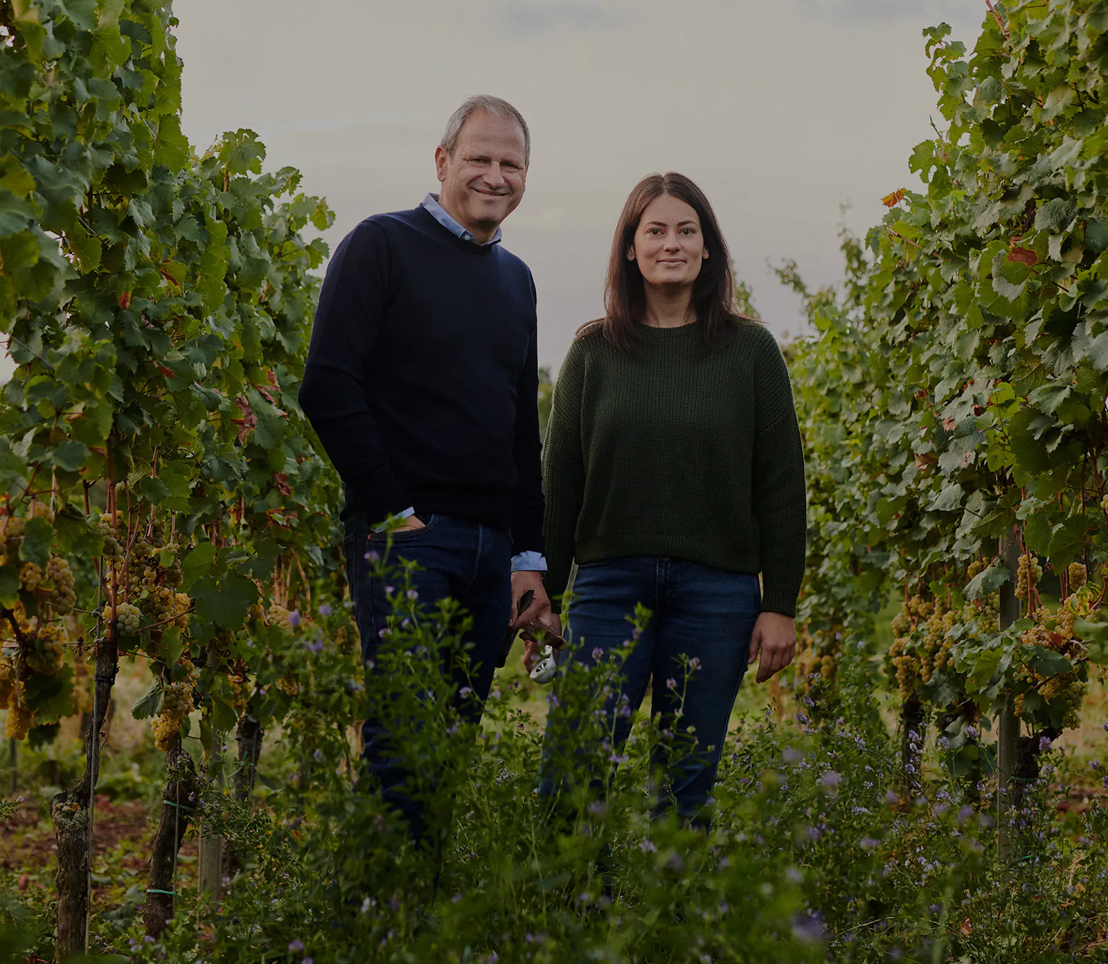 Vater Steffen und Tochter Sophie Christmann stehen zwischen Rebstöcken im Weinberg und lächeln